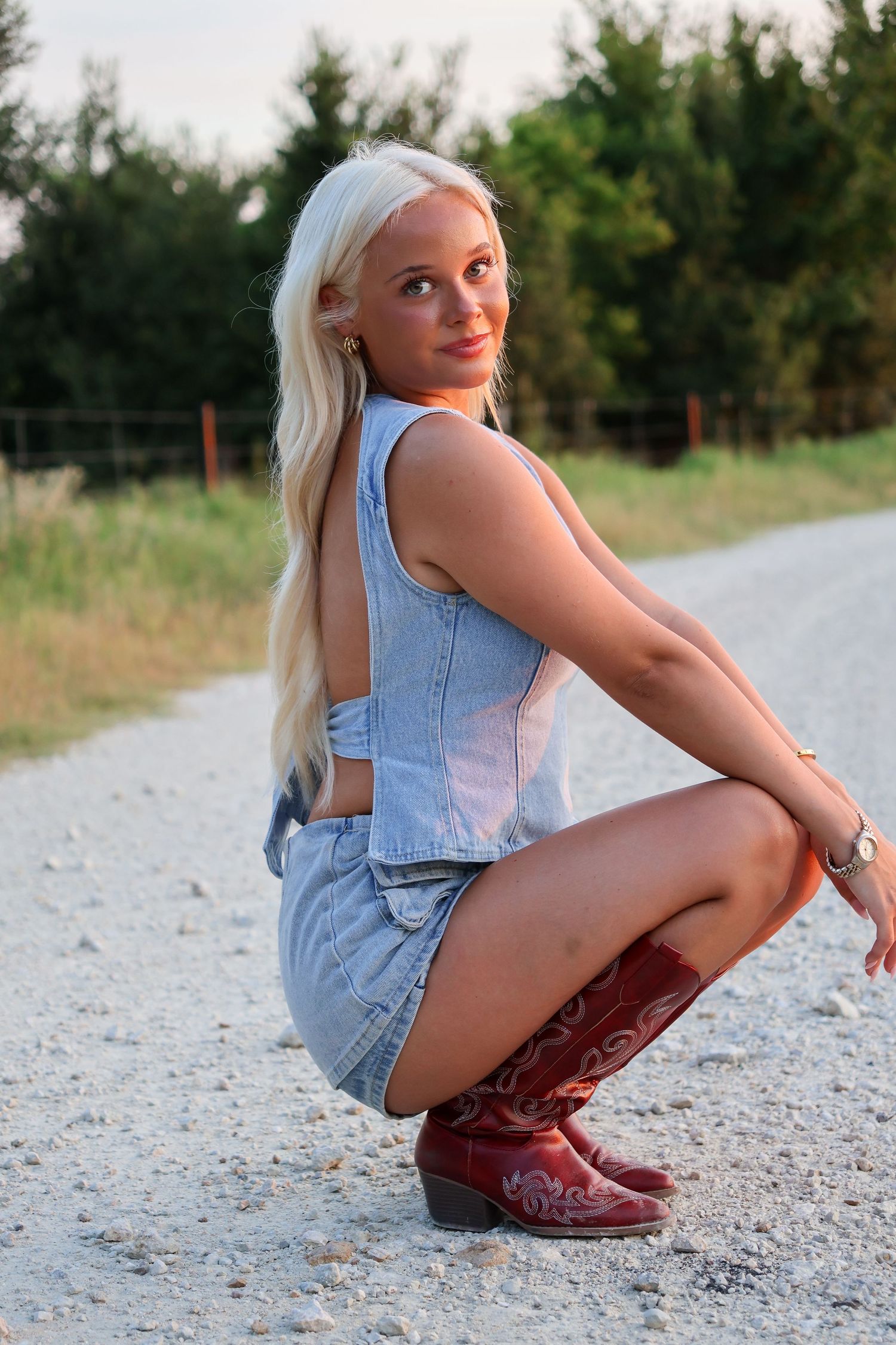 Woman in denim outfit poses on gravel path at sunset.