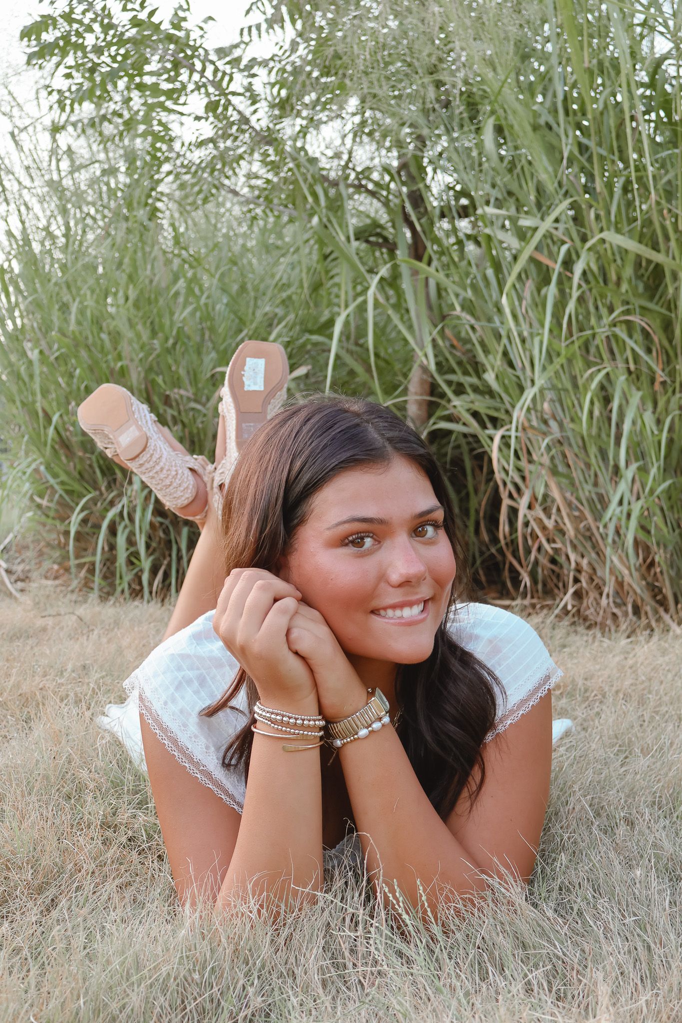 Young woman lying in tall grass wearing casual clothing and bracelets.