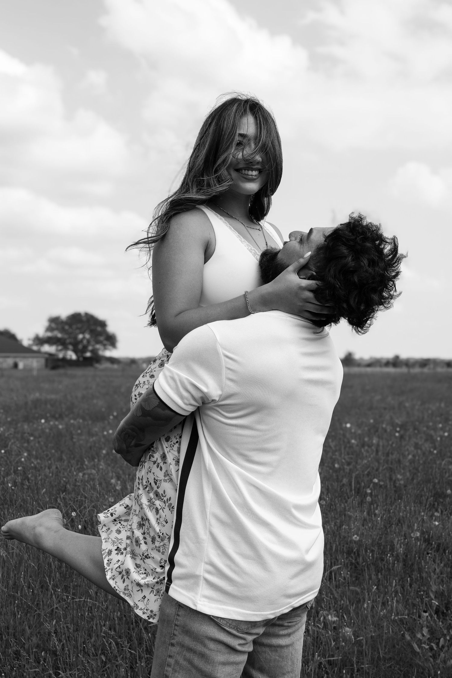 Black and white portrait of a romantic couple embracing in a field at sunset.