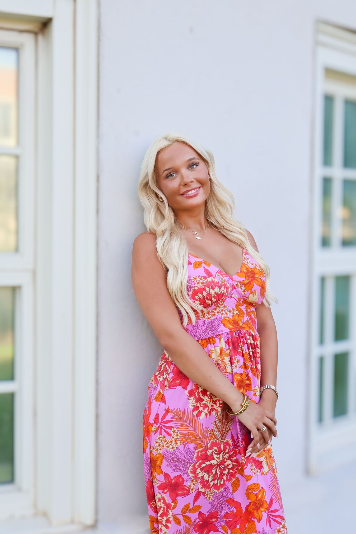Woman in vibrant pink floral maxi dress posing by white colonial architecture.