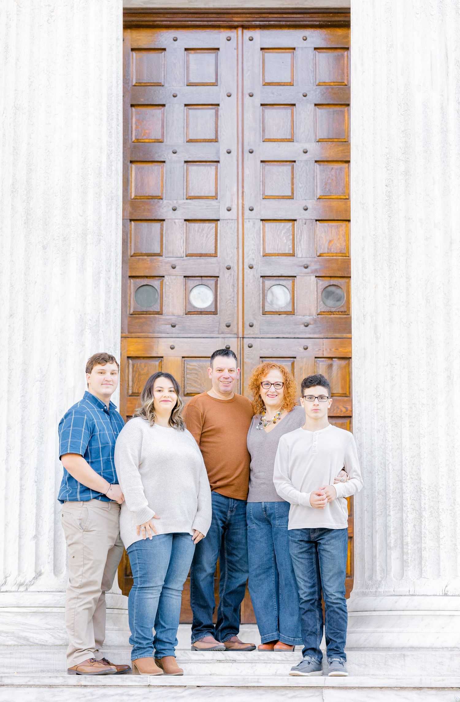 Family of five posing together in front of large wooden doors at a historic building.