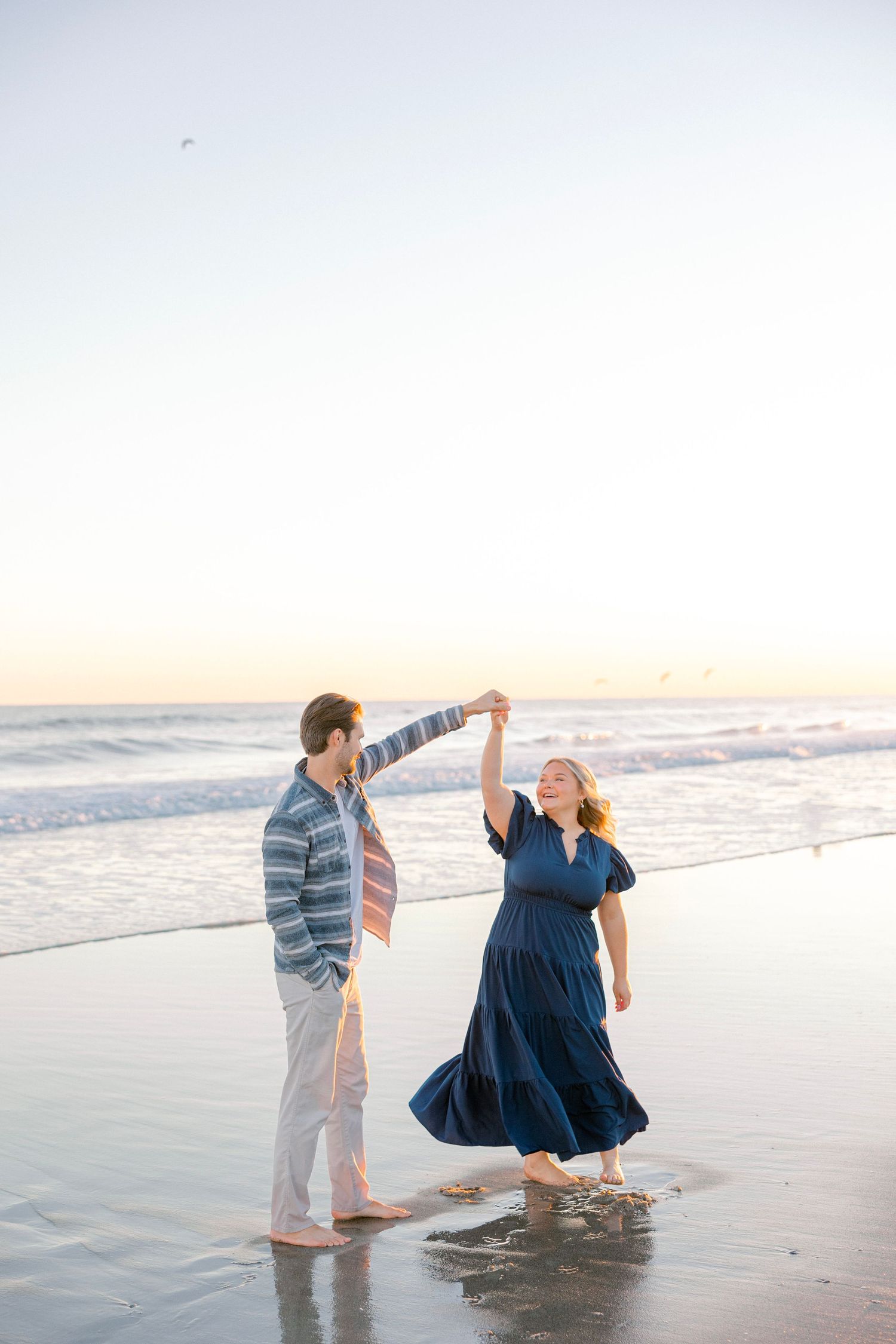 A couple plays together at the beach during golden hour in casual attire.