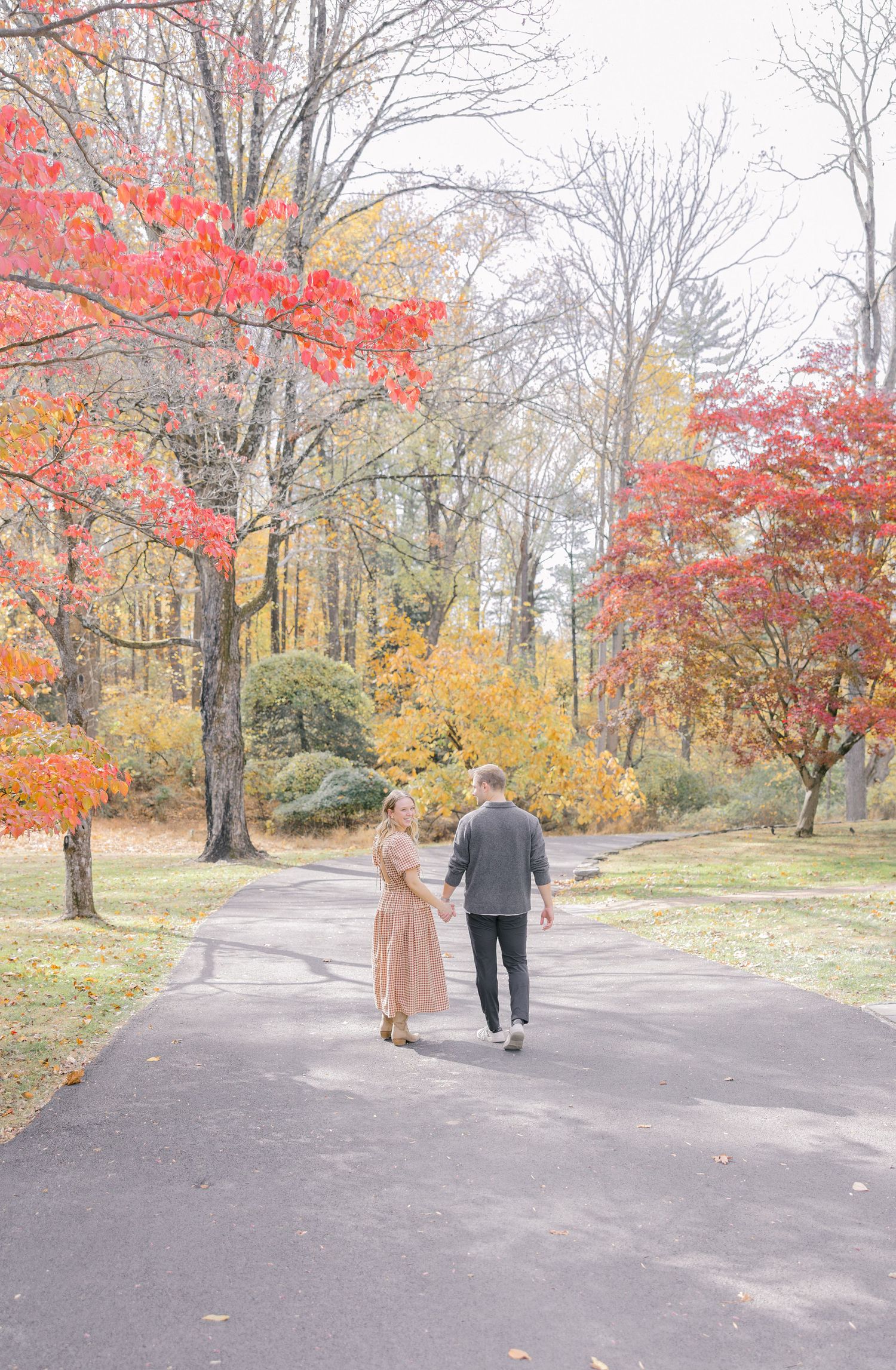 Couple holding hands walking down a path surrounded by vibrant red and yellow autumn foliage in a park.