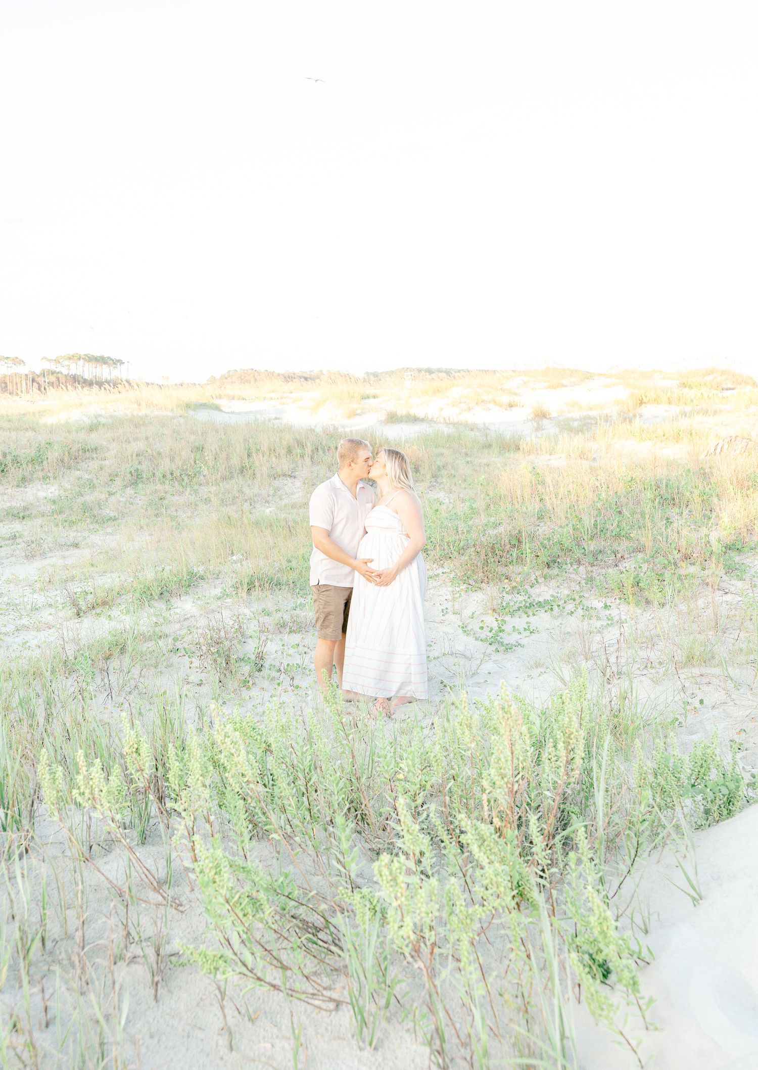 Romantic couple embraces in a dreamy beach setting with sea grass at sunset.