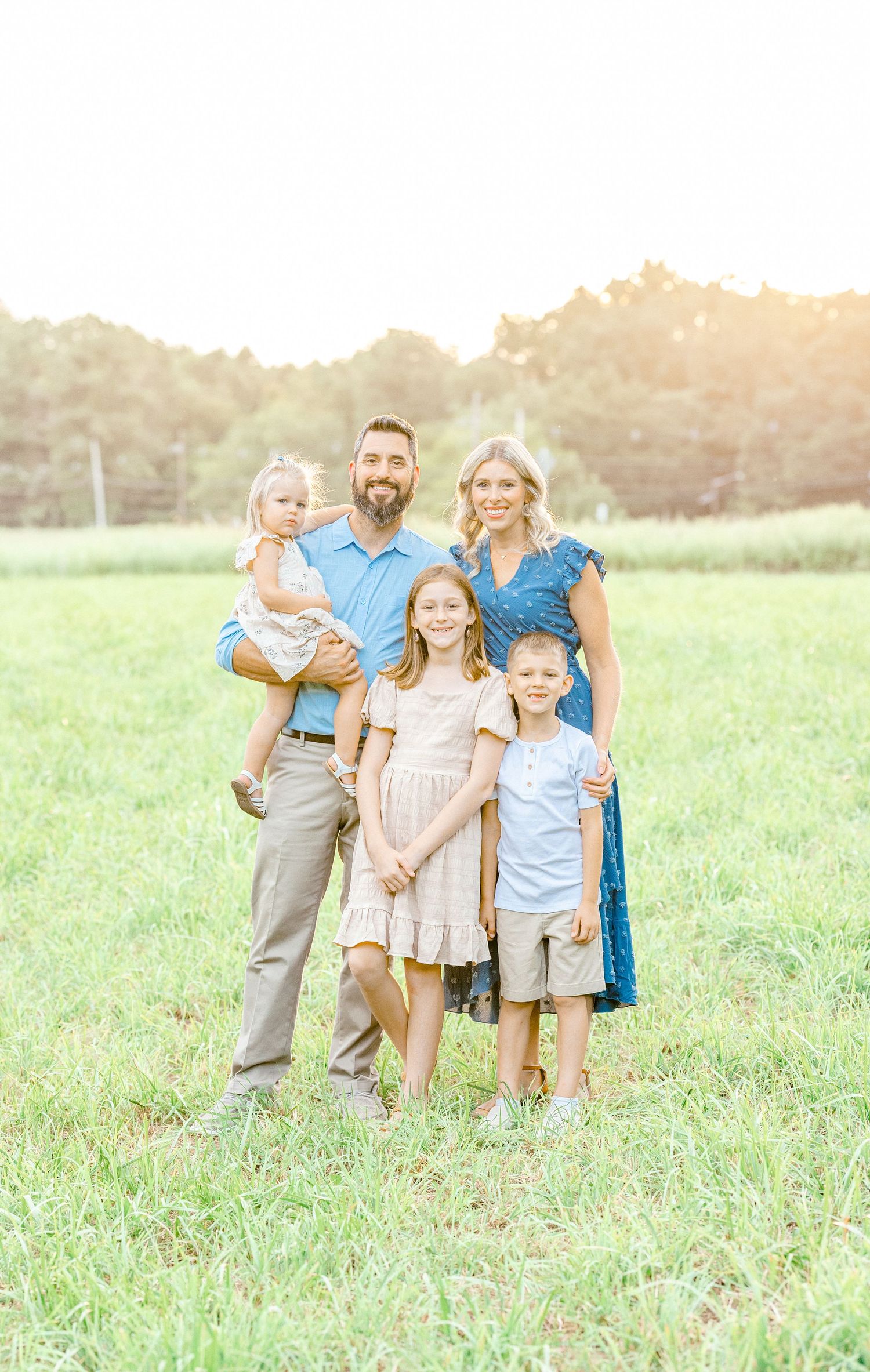 Family of five stands together in a sun-drenched meadow for portrait.