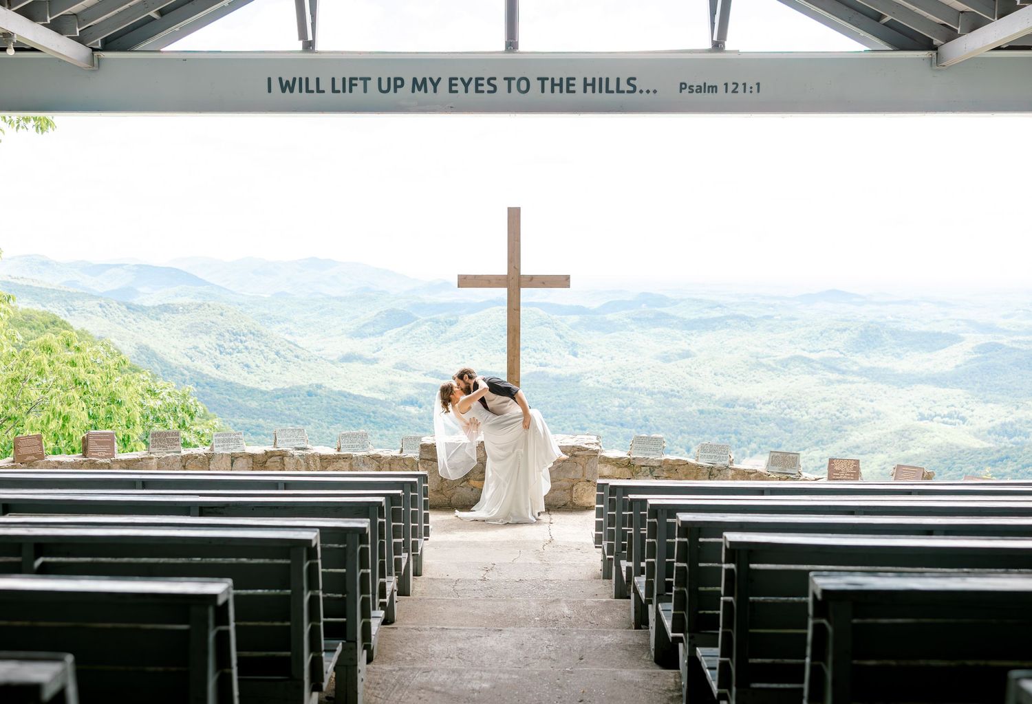 An outdoor wedding ceremony setup with wooden benches and mountain views through a scenic chapel.