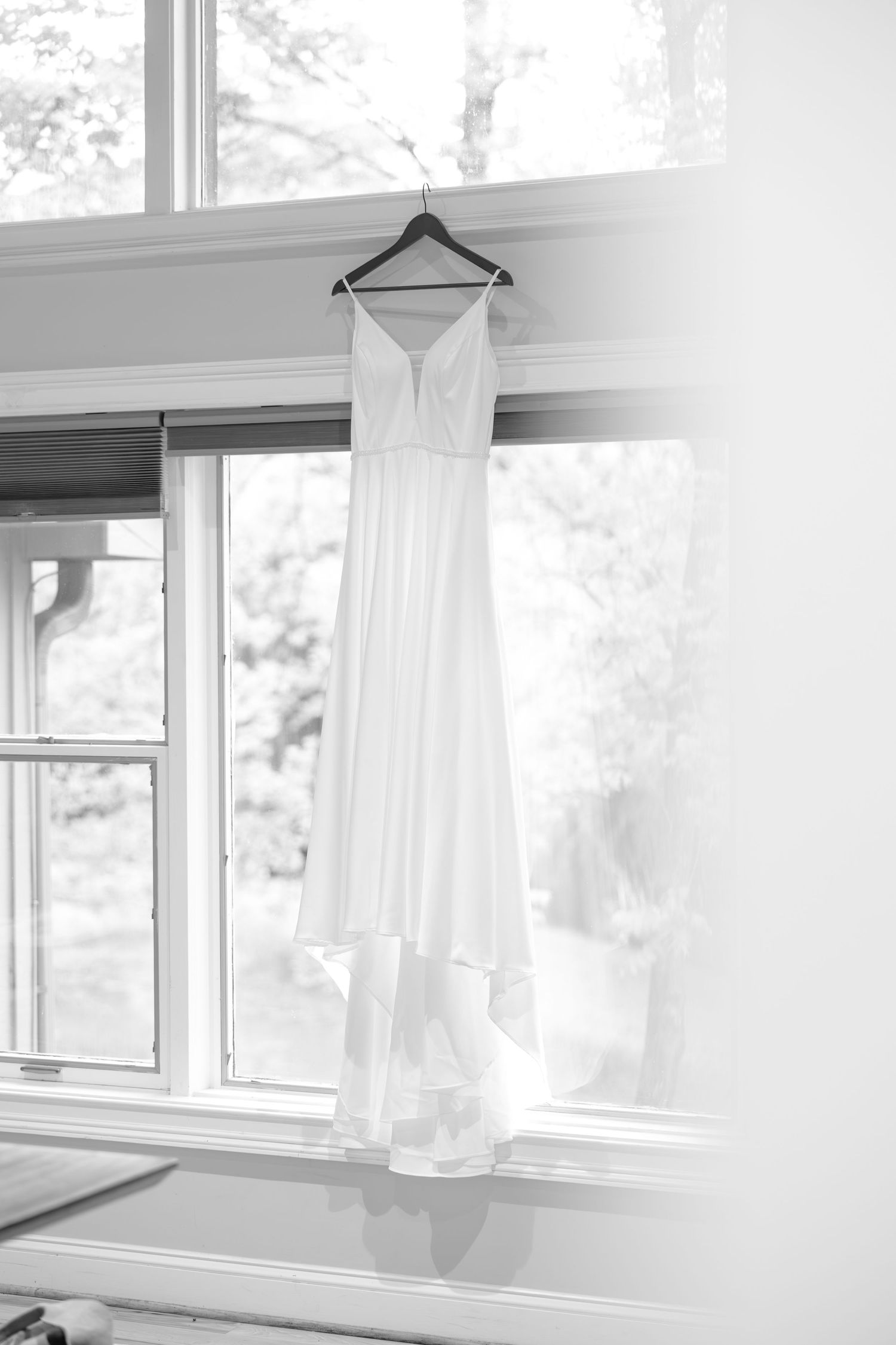 White wedding dress hanging in window light creating minimalist bridal detail.