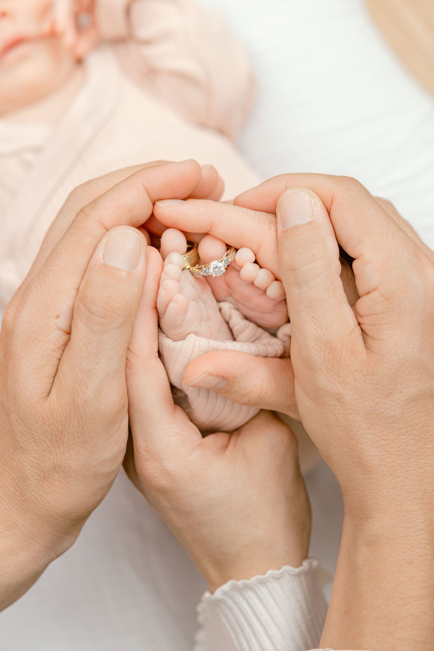 Parents cradling newborn baby feet with a diamond engagement ring resting on tiny toes.