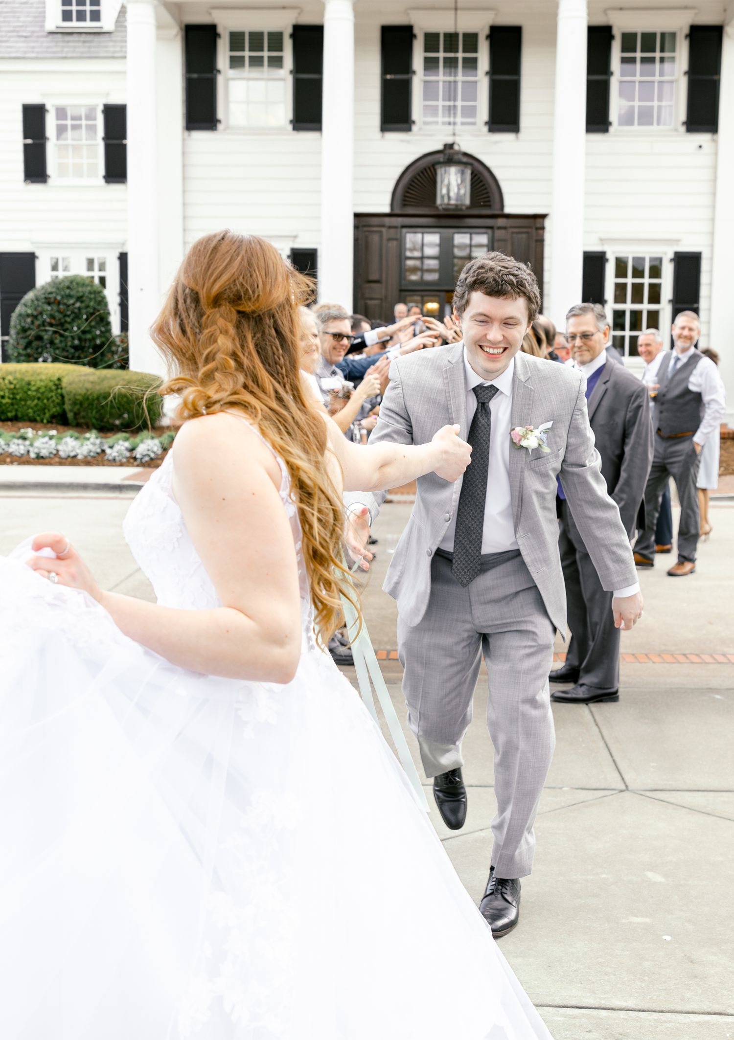 Wedding party members in gray suits dance joyfully on a white paved area.