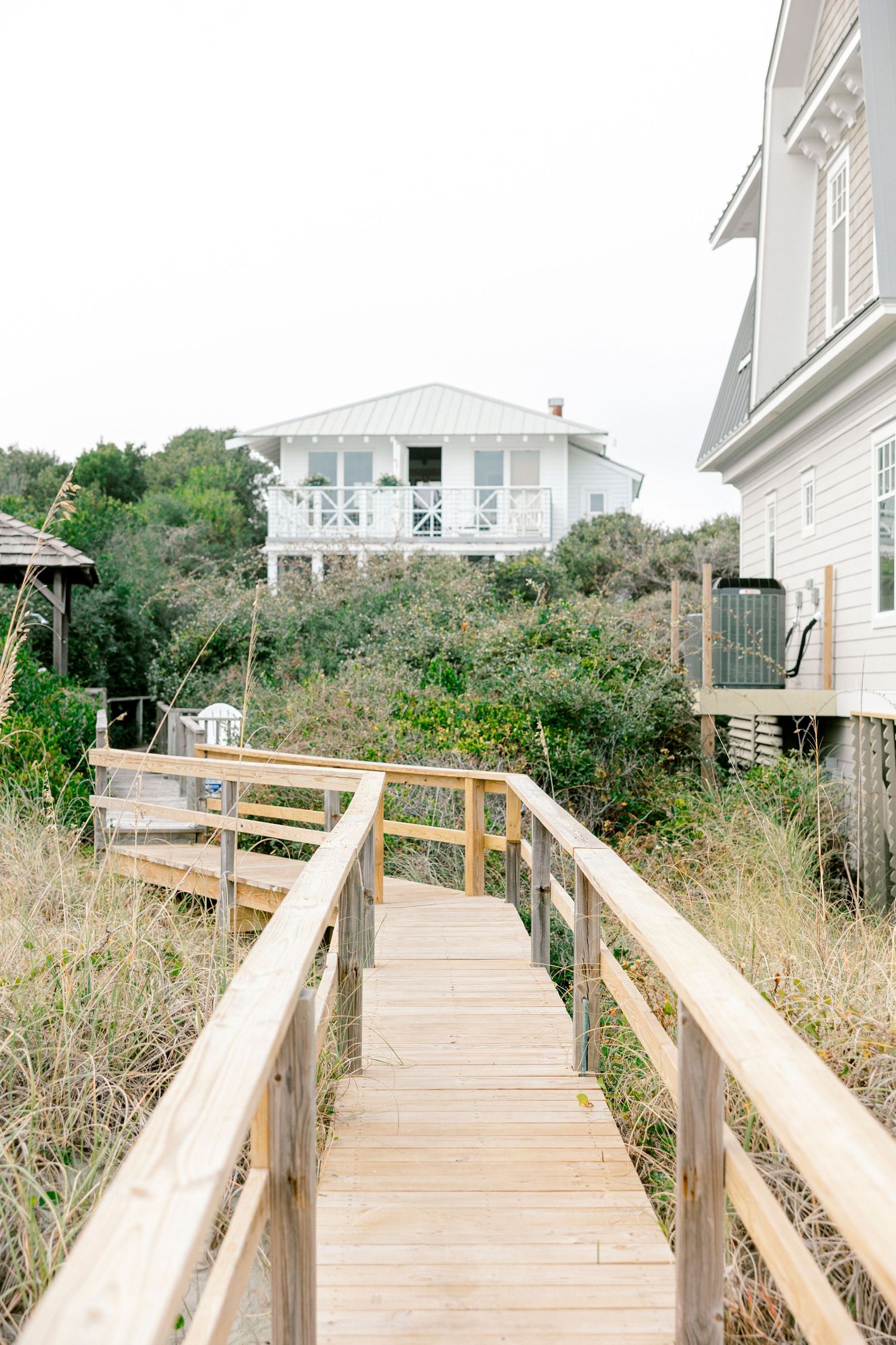 Wooden boardwalk leading to beach houses along the coast with natural vegetation.