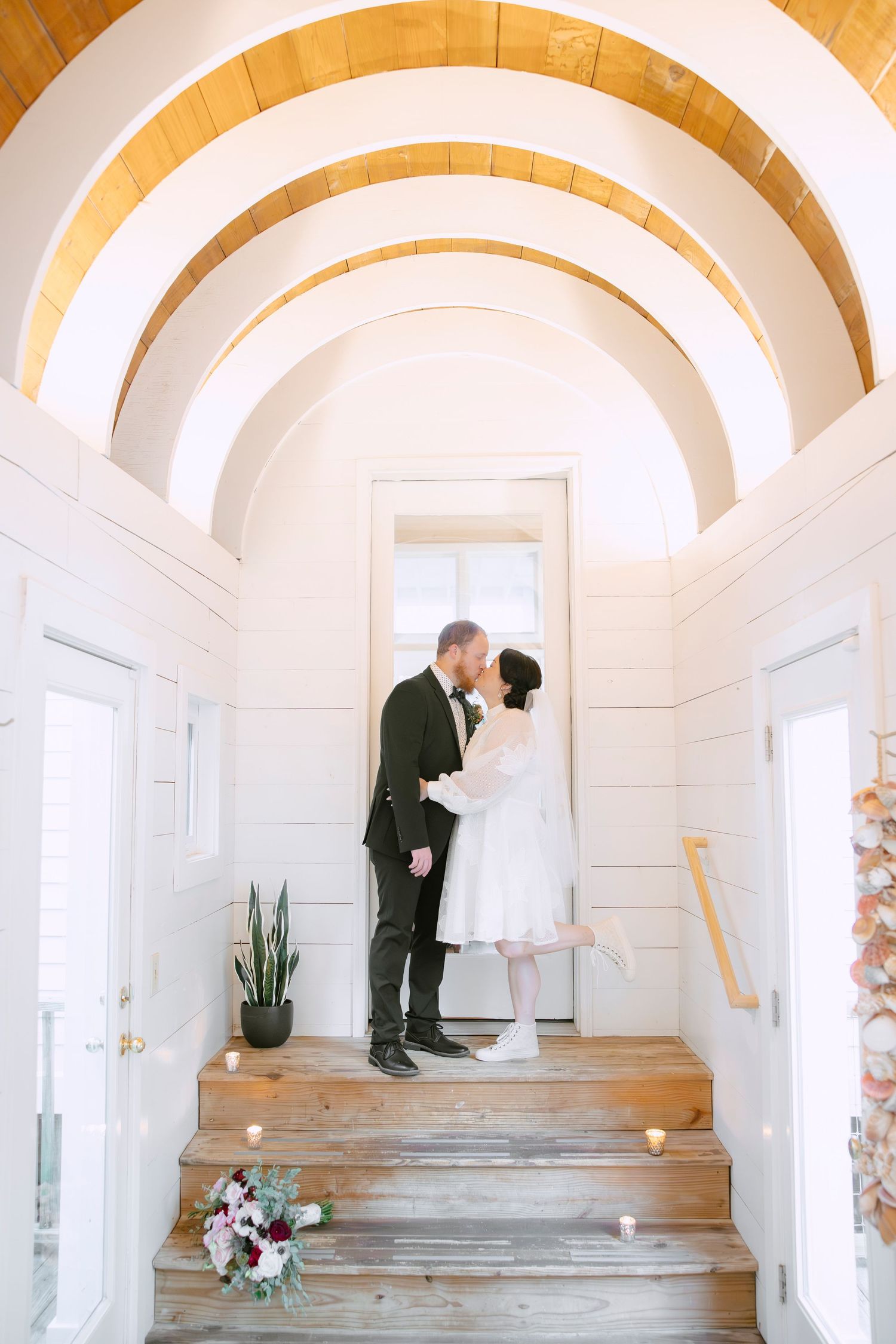 Wedding couple shares intimate moment in arched hallway with wooden barrel ceiling.