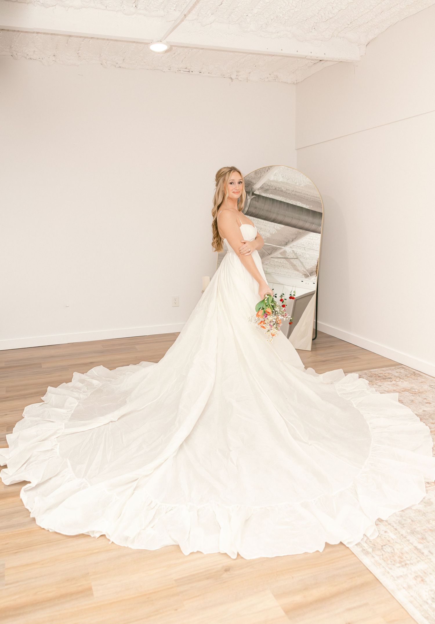 Bride in strapless ball gown wedding dress with cathedral train holding floral bouquet in bright white studio.
