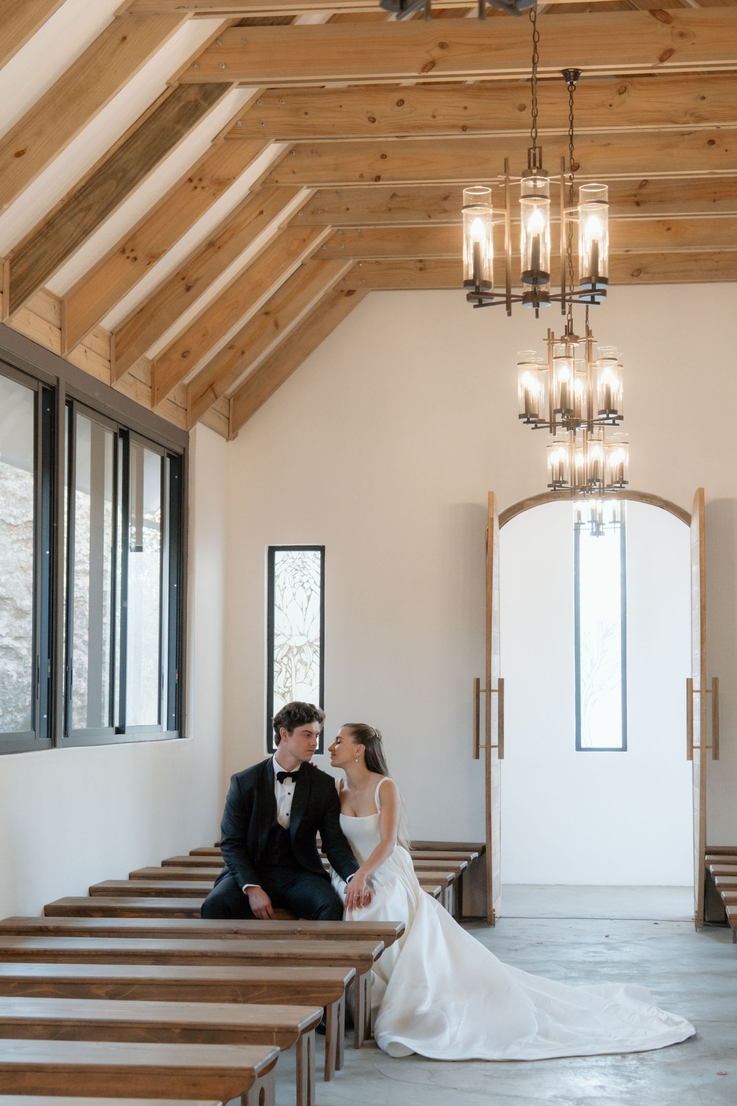 Bride and groom sitting together in a modern rustic chapel with vaulted wood ceiling and chandelier.