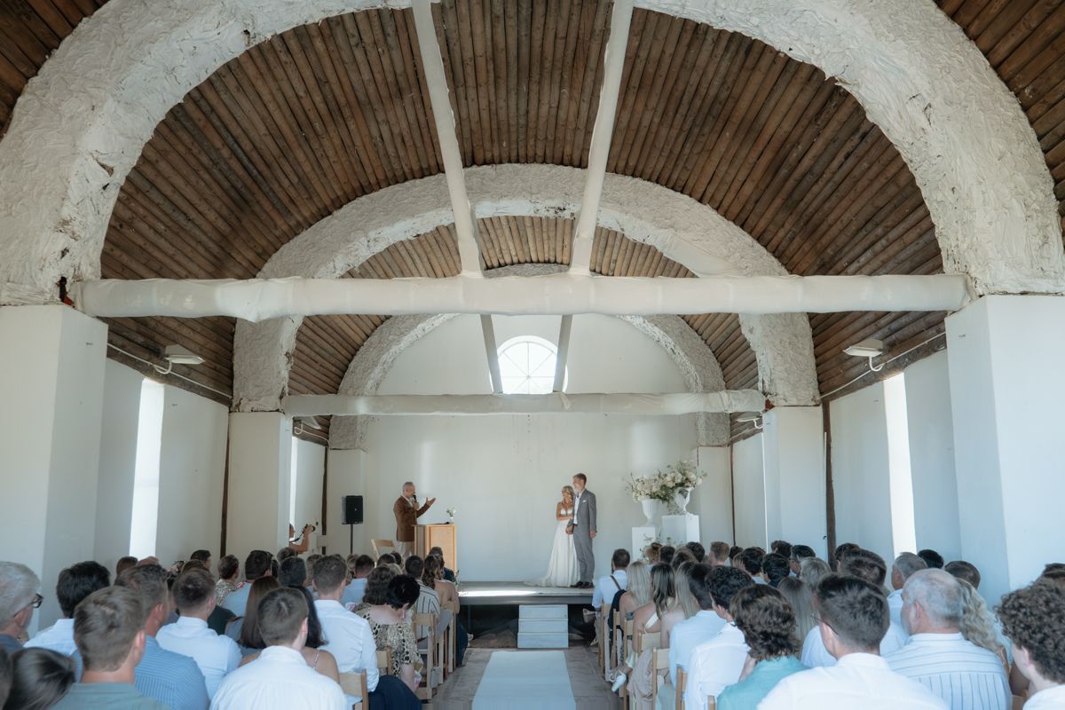 Wedding ceremony inside a rustic arched venue with wooden ceiling and seated guests.