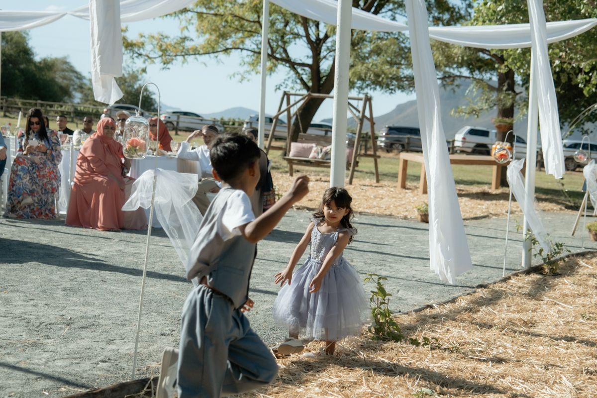 Two young girls in dresses play near mirrored panels at an outdoor wedding ceremony setup.