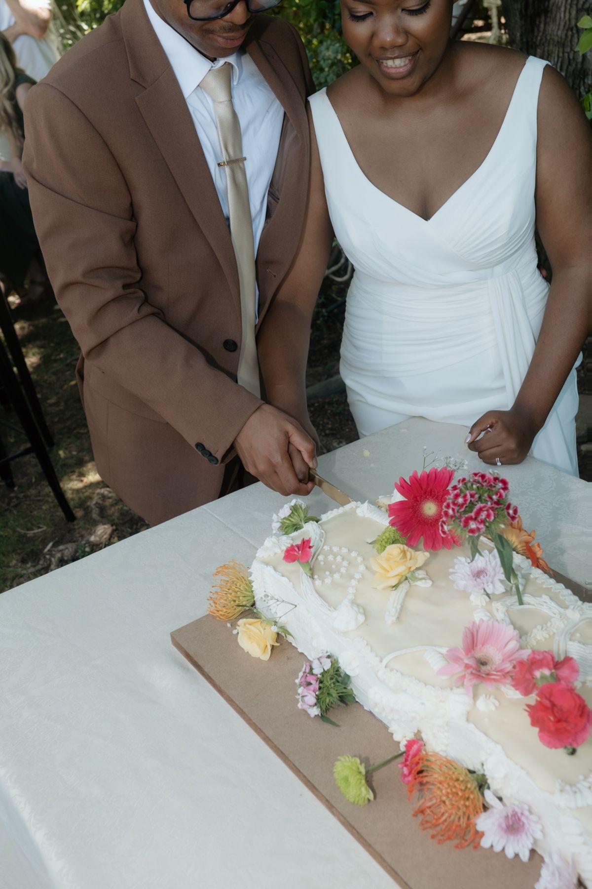 Bride and groom cutting a floral-decorated wedding cake at an outdoor reception.