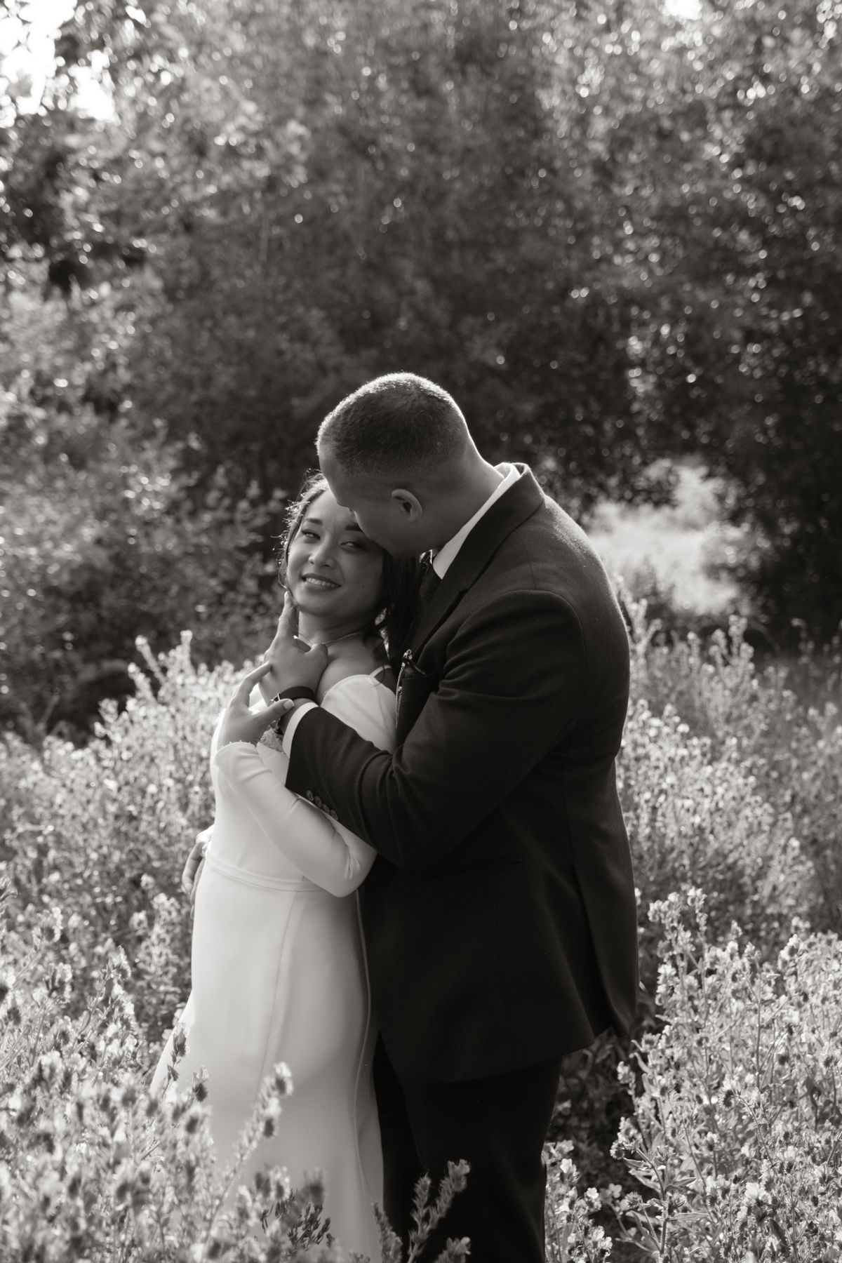 Black and white romantic portrait of bride and groom embracing in flowering garden at wedding.