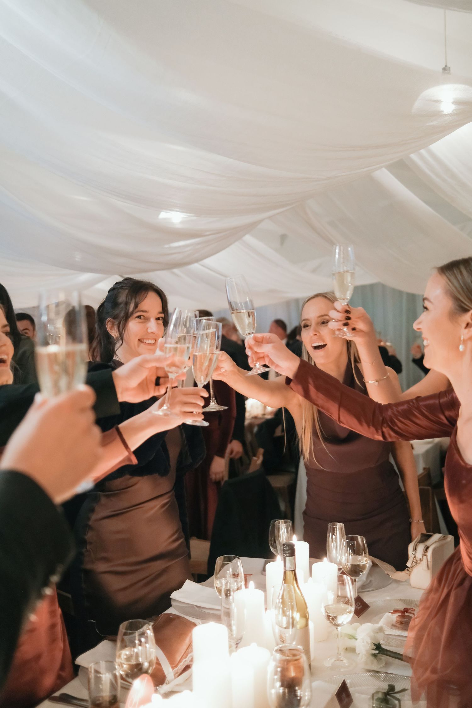 Wedding guests raise champagne glasses in a toast under elegant white draped ceiling at reception.