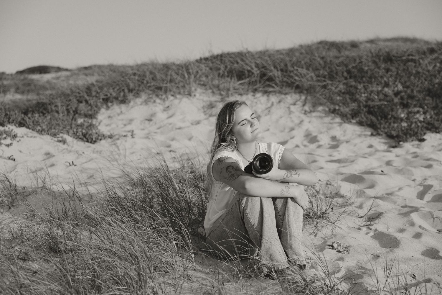 A black and white panoramic view of sand dunes with tall grass and figures walking along the beach.