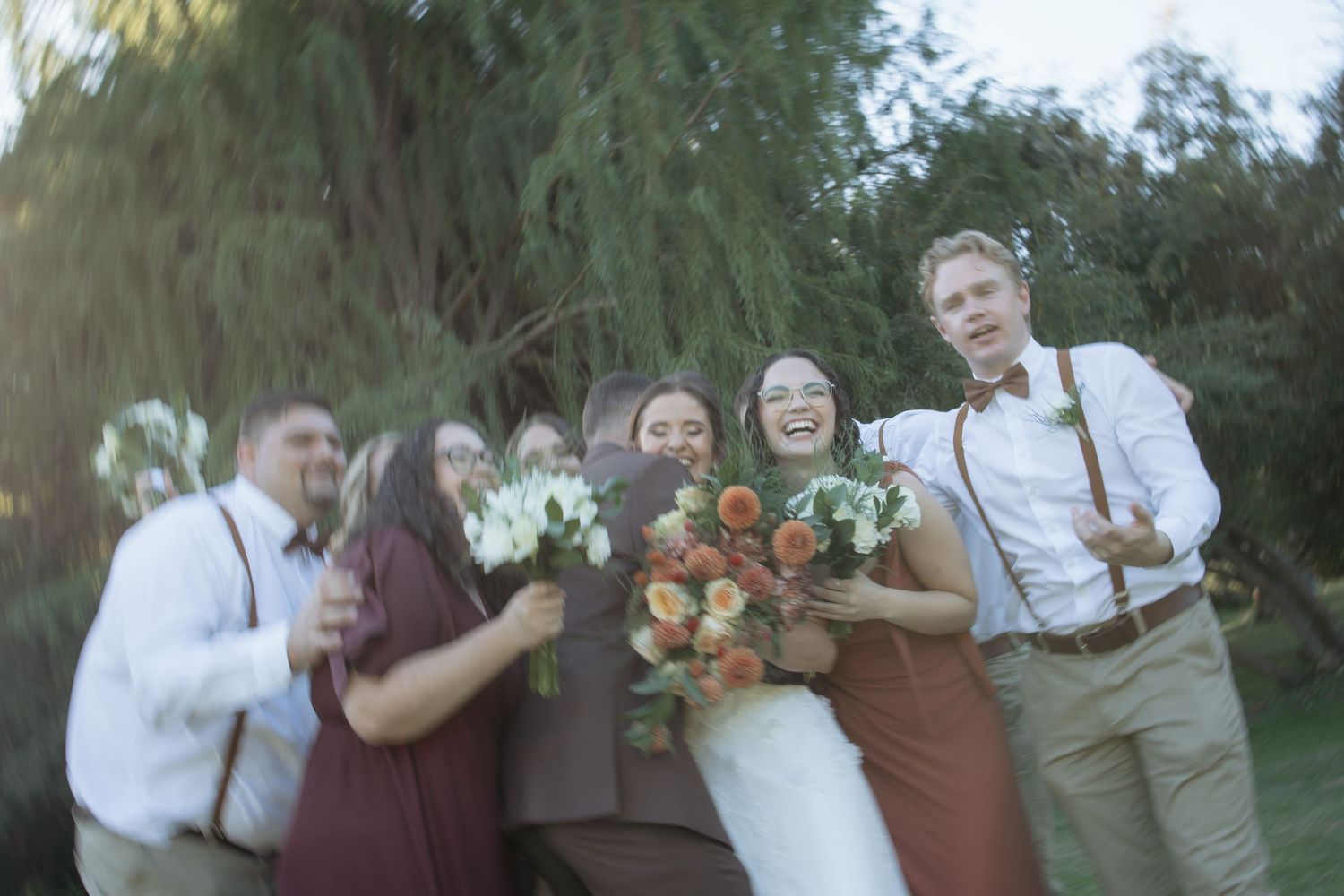 Joyful wedding party laughs and celebrates outdoors holding colorful bridal bouquets.