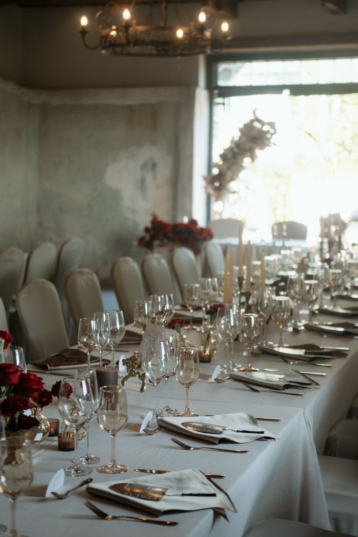 Sophisticated wedding banquet table featuring crystal glassware, candles, and deep red rose centerpieces.