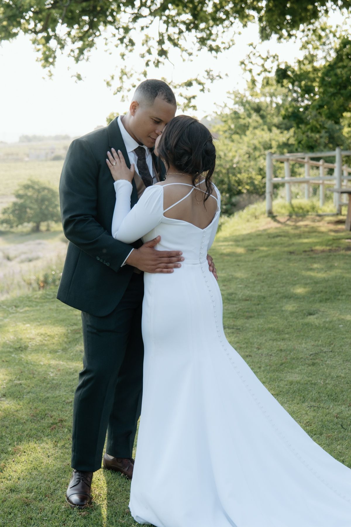 Bride and groom share an intimate embrace outdoors in golden hour light, bride in long-sleeved white gown with train.