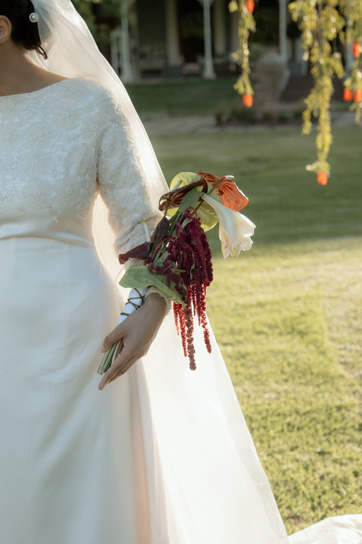 Bride in long-sleeve lace wedding gown holding dramatic burgundy and green cascading bouquet.