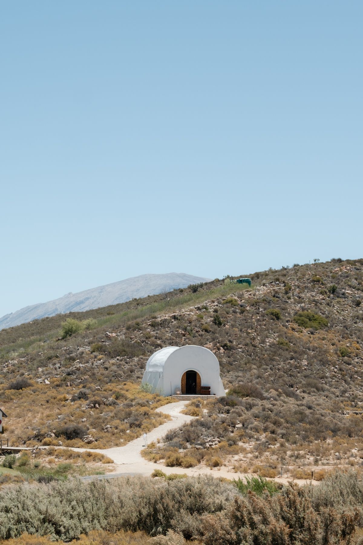 A white dome-shaped structure on a arid hillside with a winding path leading to its arched wooden door.