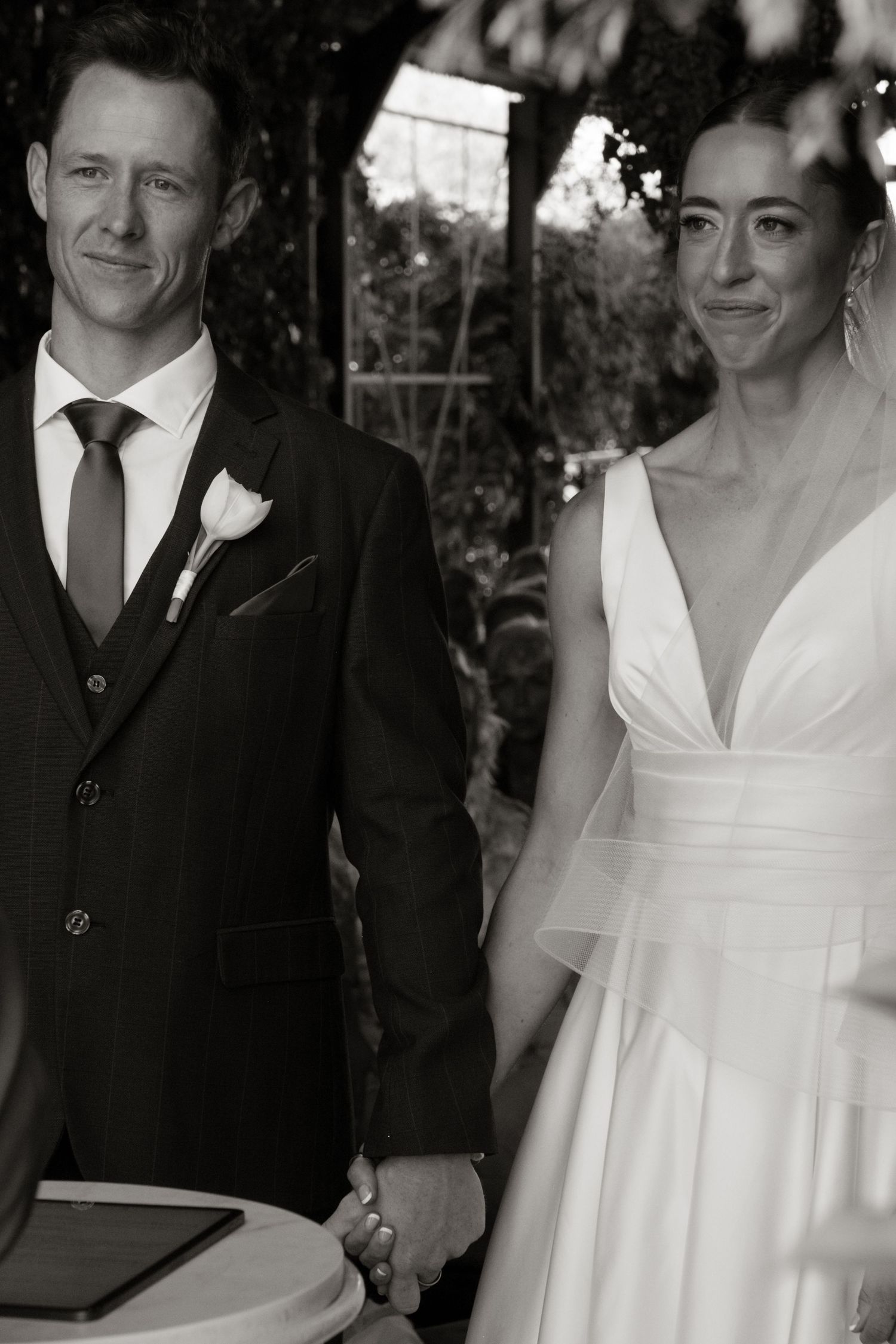 Black and white photo of bride and groom holding hands during wedding ceremony.