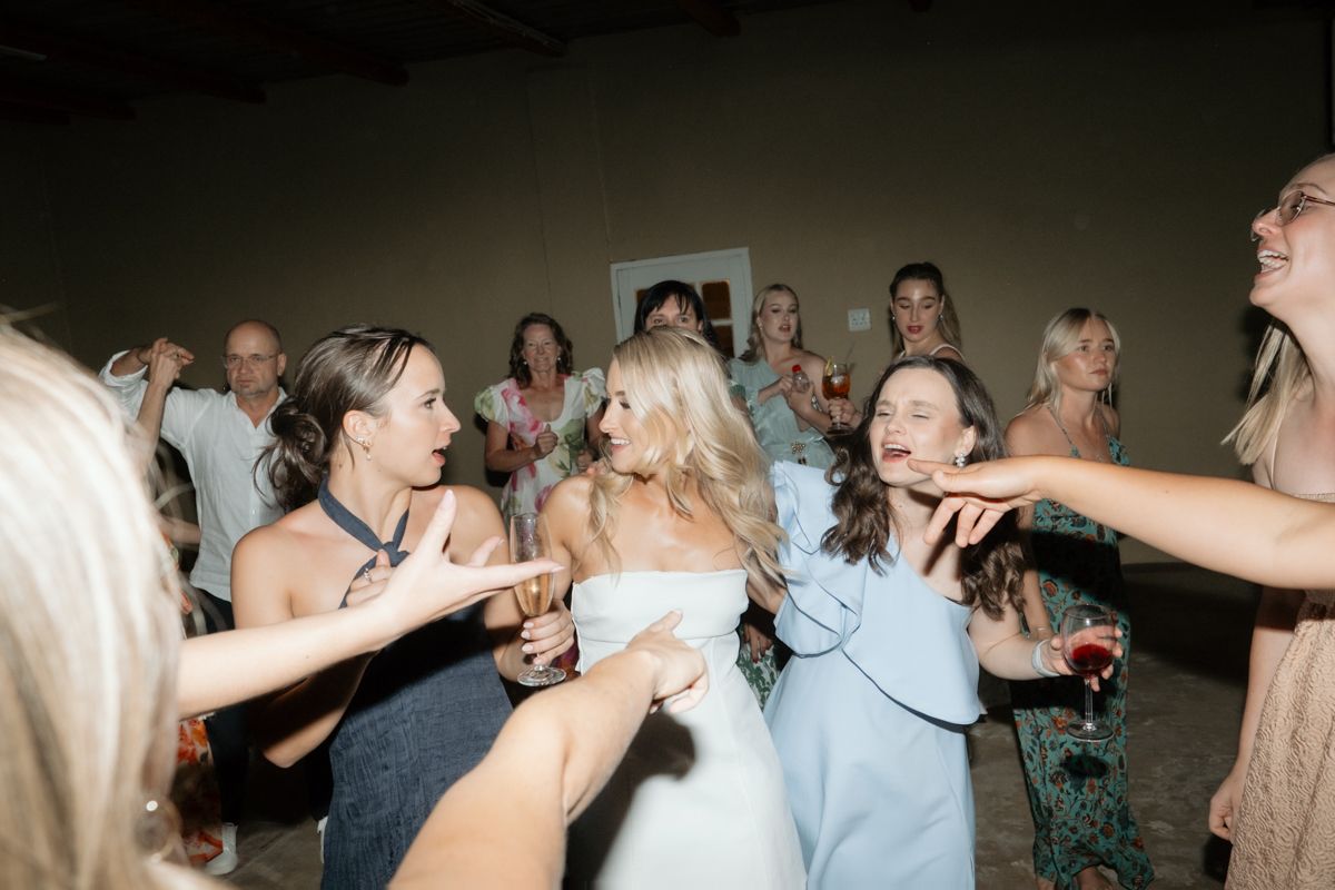 Blonde bride dances joyfully surrounded by celebrating guests at lively wedding reception party.