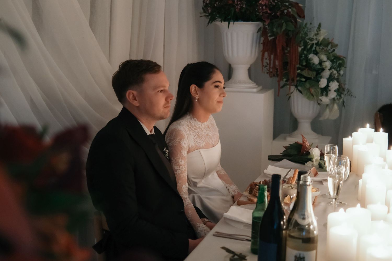 Bride and groom sit together at candlelit wedding reception table in elegant venue.