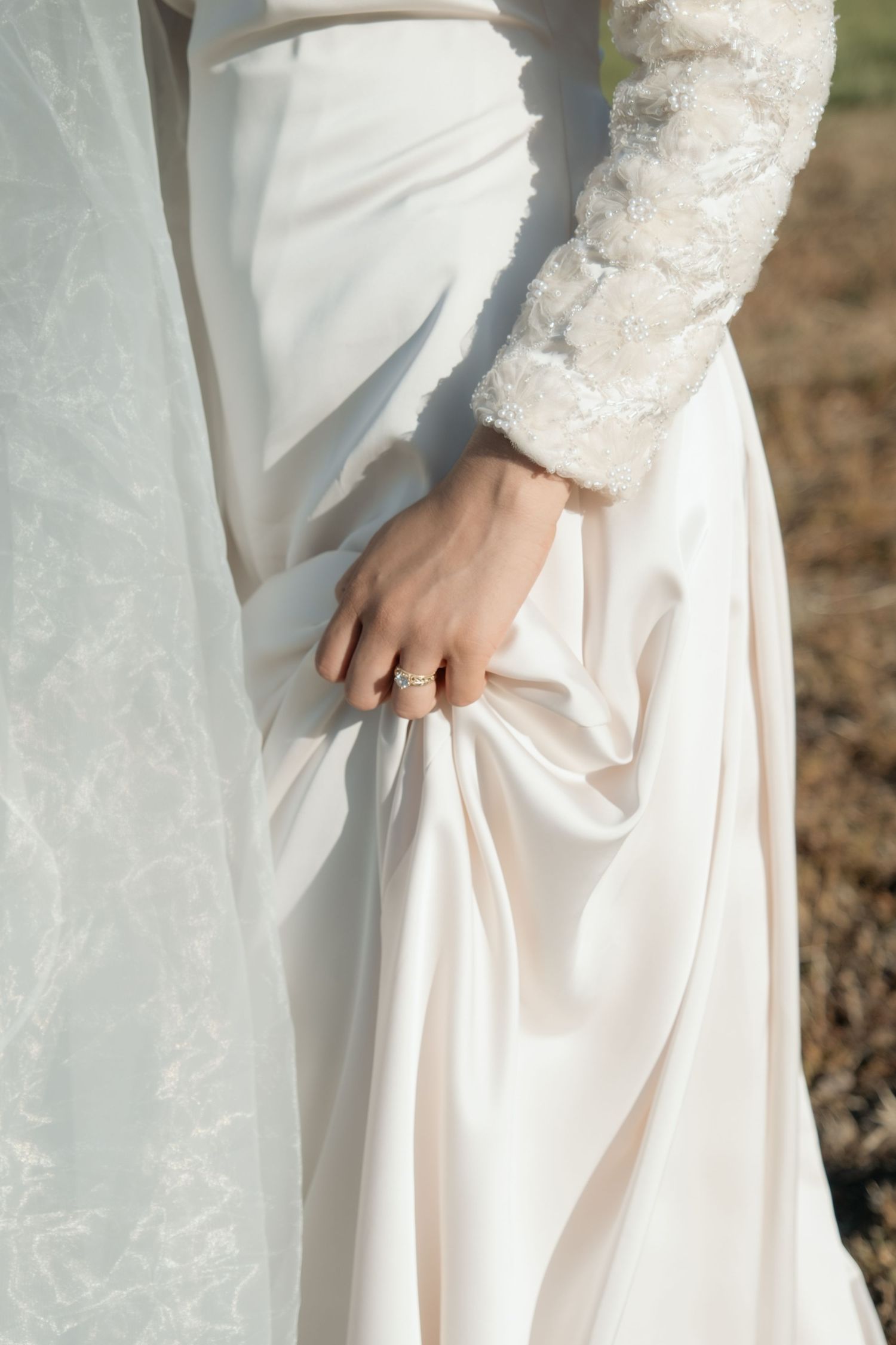 Close-up of bride holding white satin wedding dress with diamond ring on her hand.