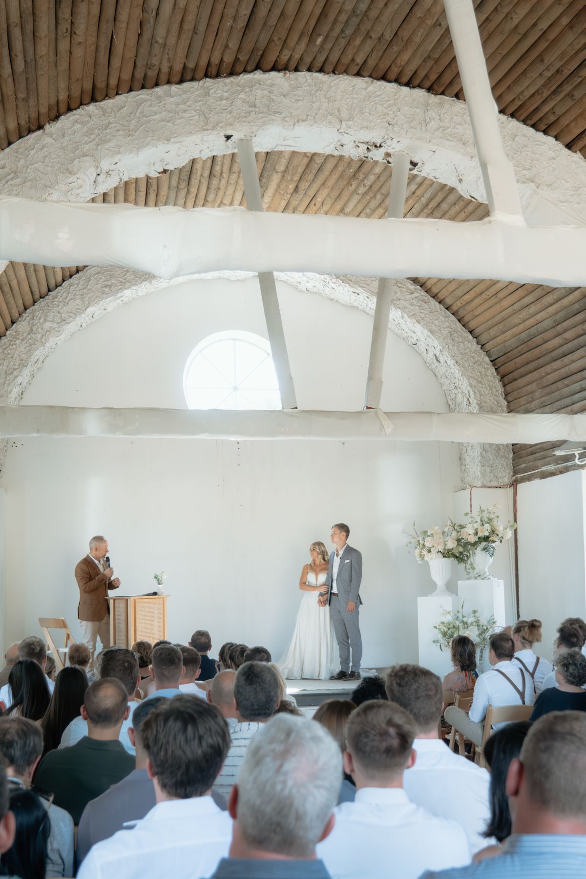 Wedding ceremony inside a rustic white chapel with arched ceiling and guests seated in rows.