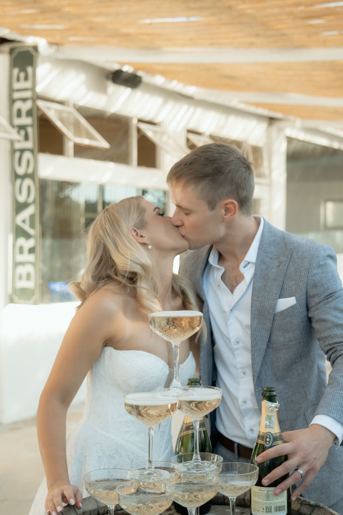 Bride and groom kissing beside champagne tower outside a Brasserie venue at their wedding.