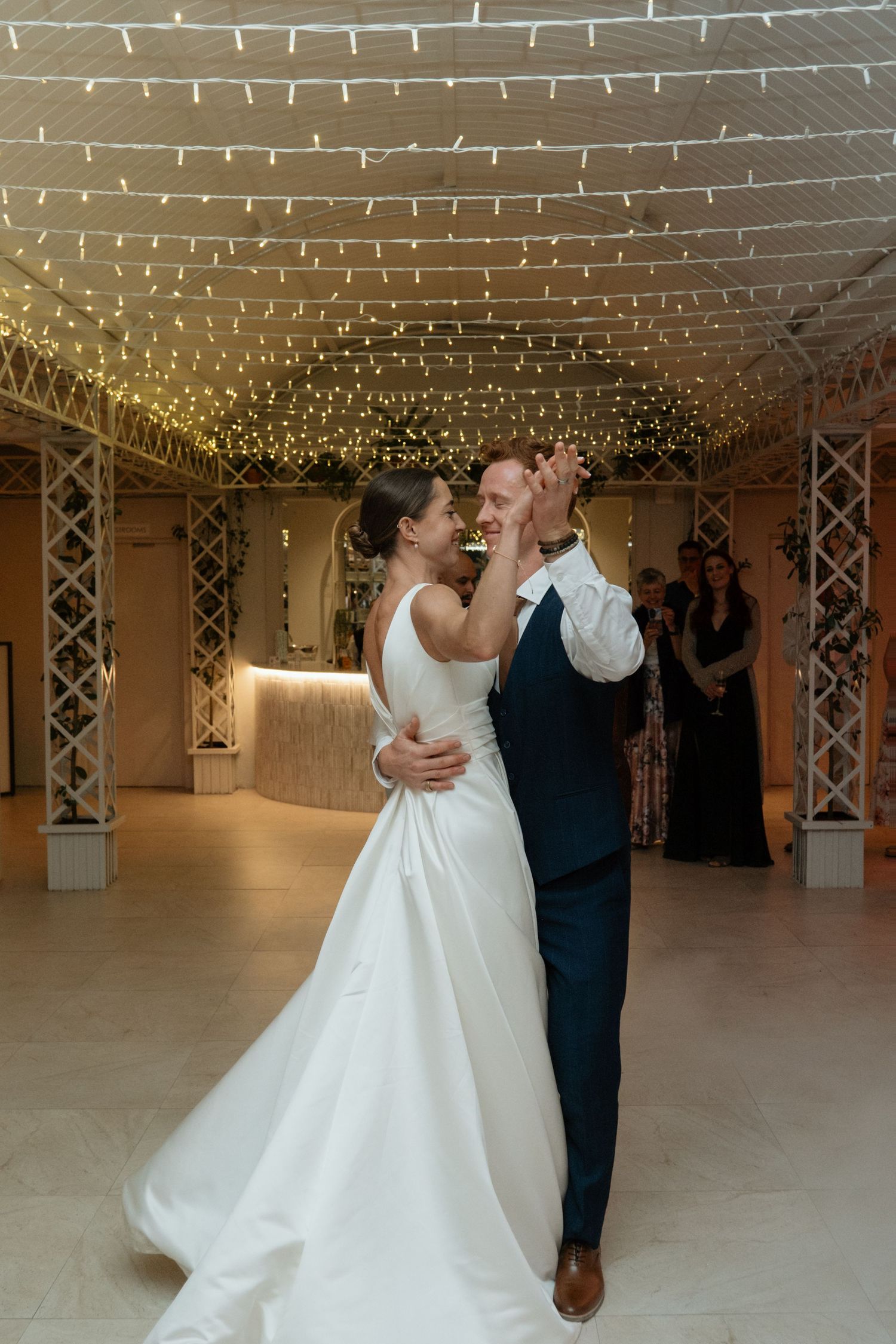Bride and groom share their first dance under twinkling fairy lights in an elegant wedding venue.