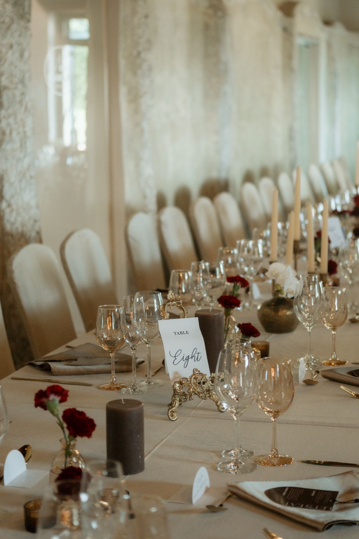Elegant wedding reception table setup with white linens, crystal glasses, candles, and red floral centerpieces.
