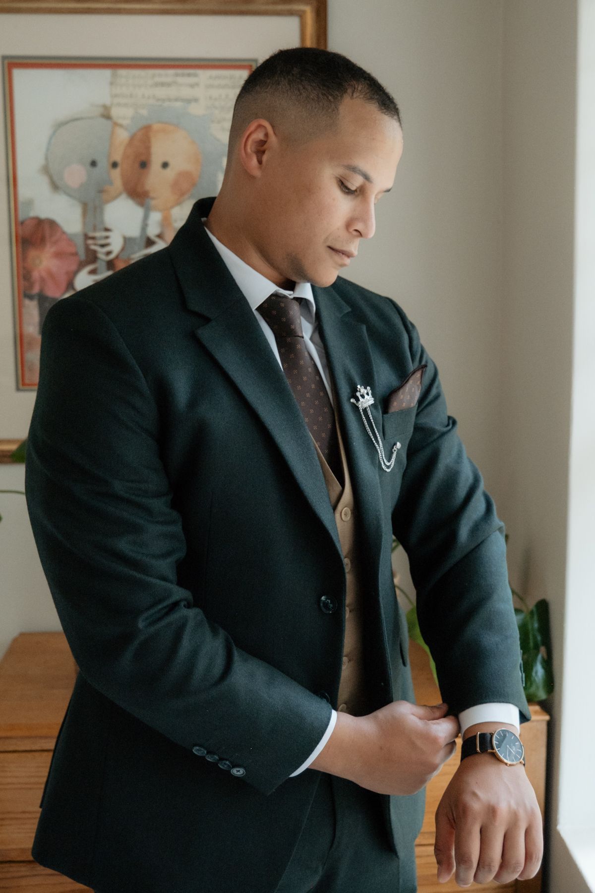 Dapper groom in dark green suit with boutonniere and watch checks his cufflinks before wedding ceremony.