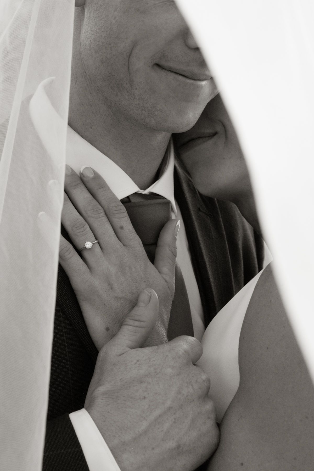 Black and white close-up of bride and groom embracing, showcasing a diamond engagement ring on her hand.