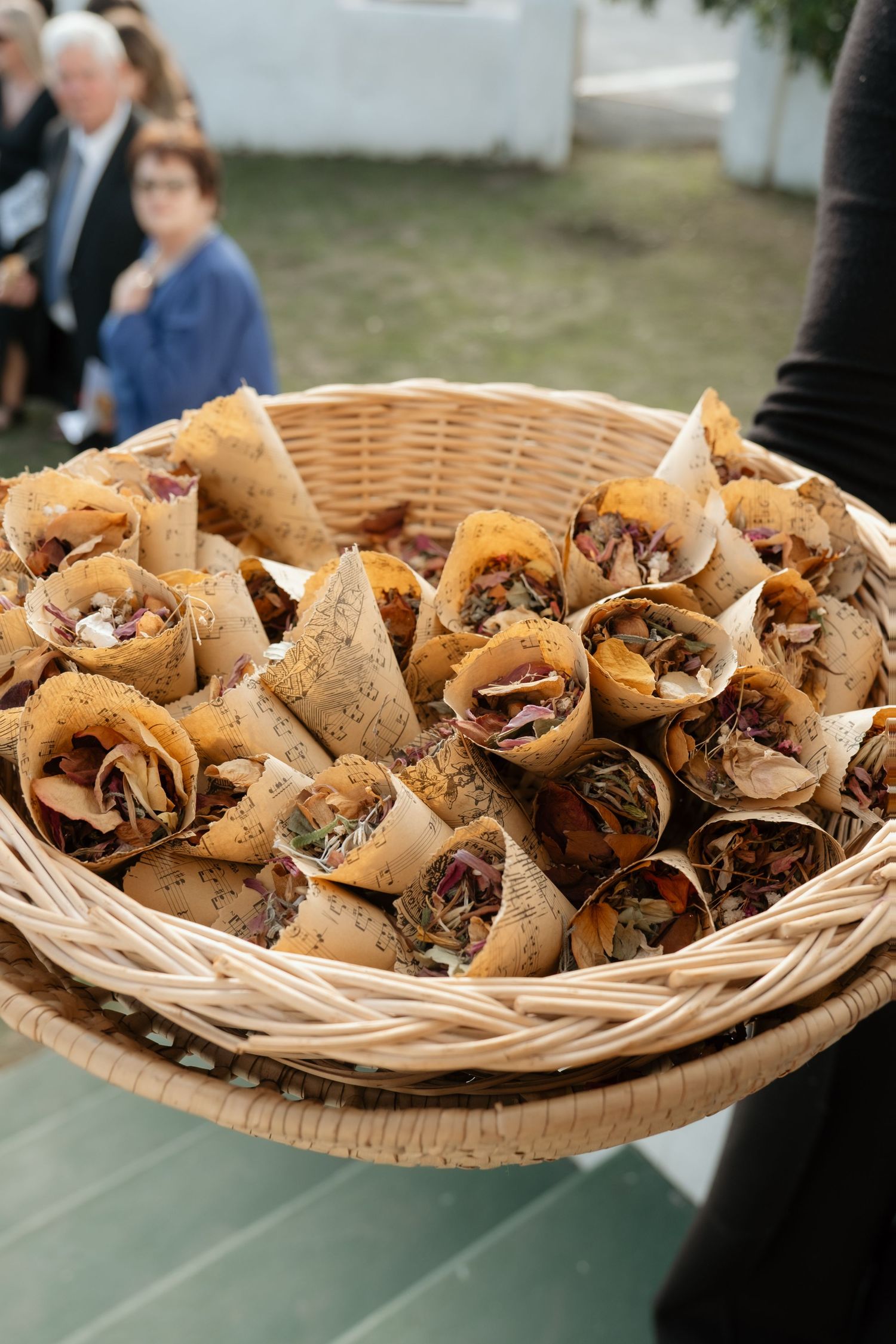 Wicker basket filled with paper cone wedding favors containing dried flower petals for tossing at a ceremony.
