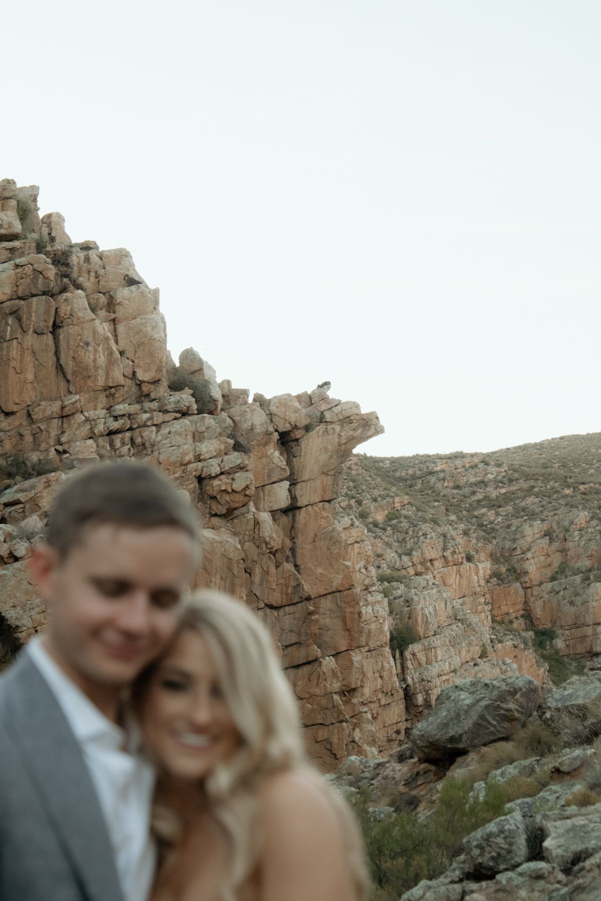 Newlywed couple smiling together with dramatic rocky canyon landscape in the background.