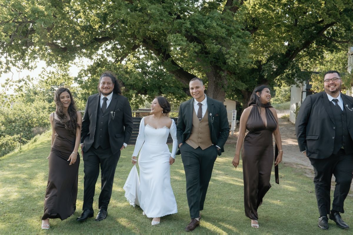Wedding party of six walking together under a large tree on a sunny day.