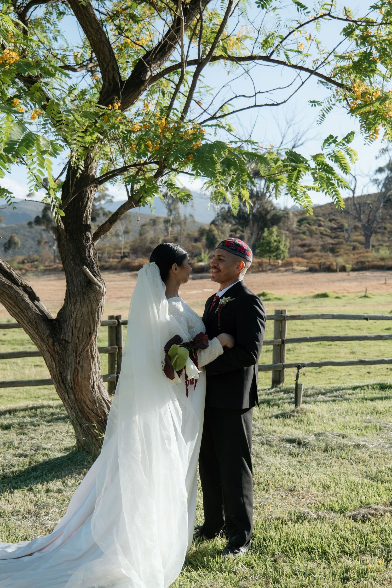 Bride and groom share a romantic moment under a tree at their outdoor farm wedding ceremony.