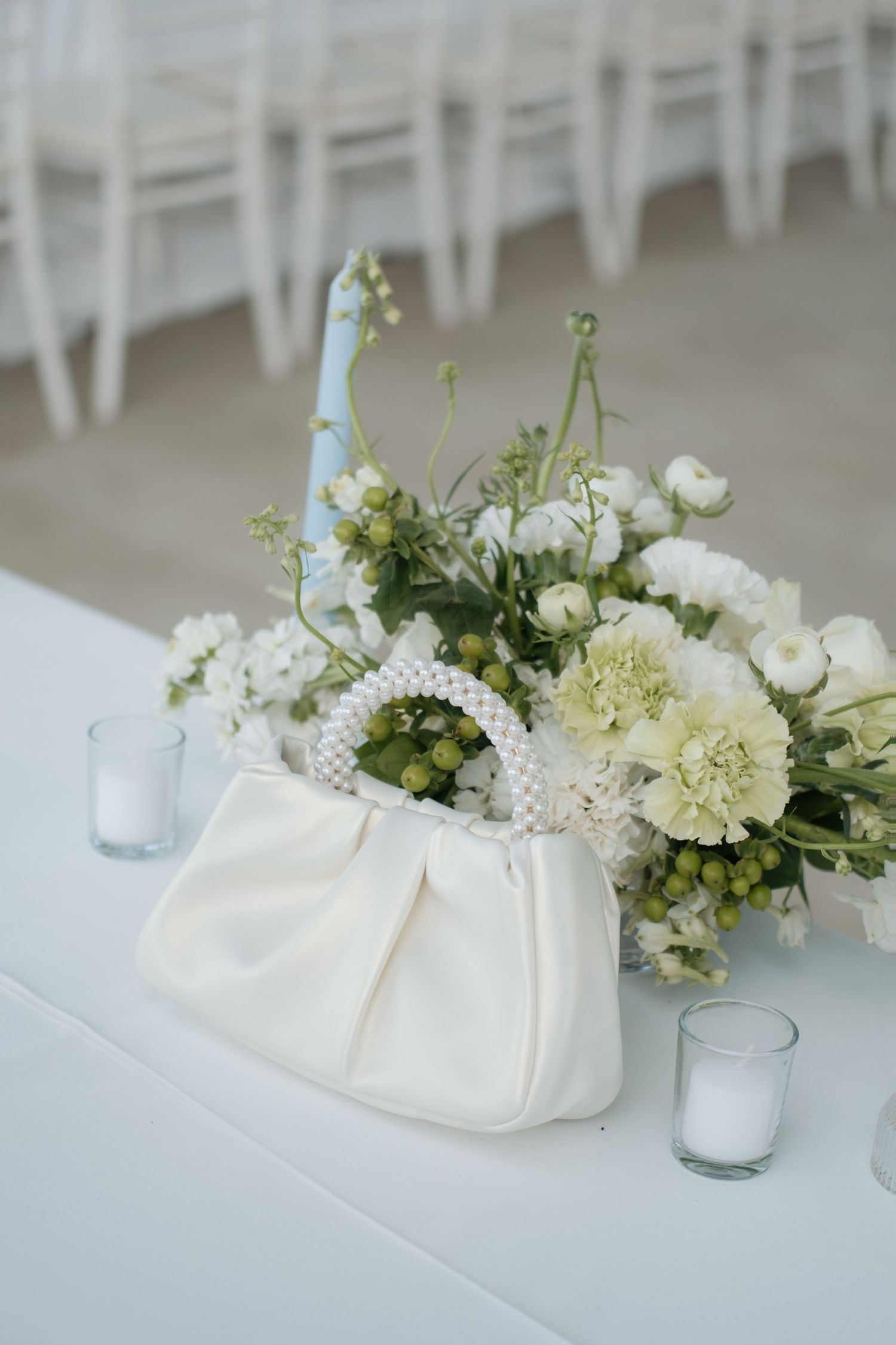 Elegant white floral centerpiece with greenery arranged on a white tablecloth for a wedding reception.