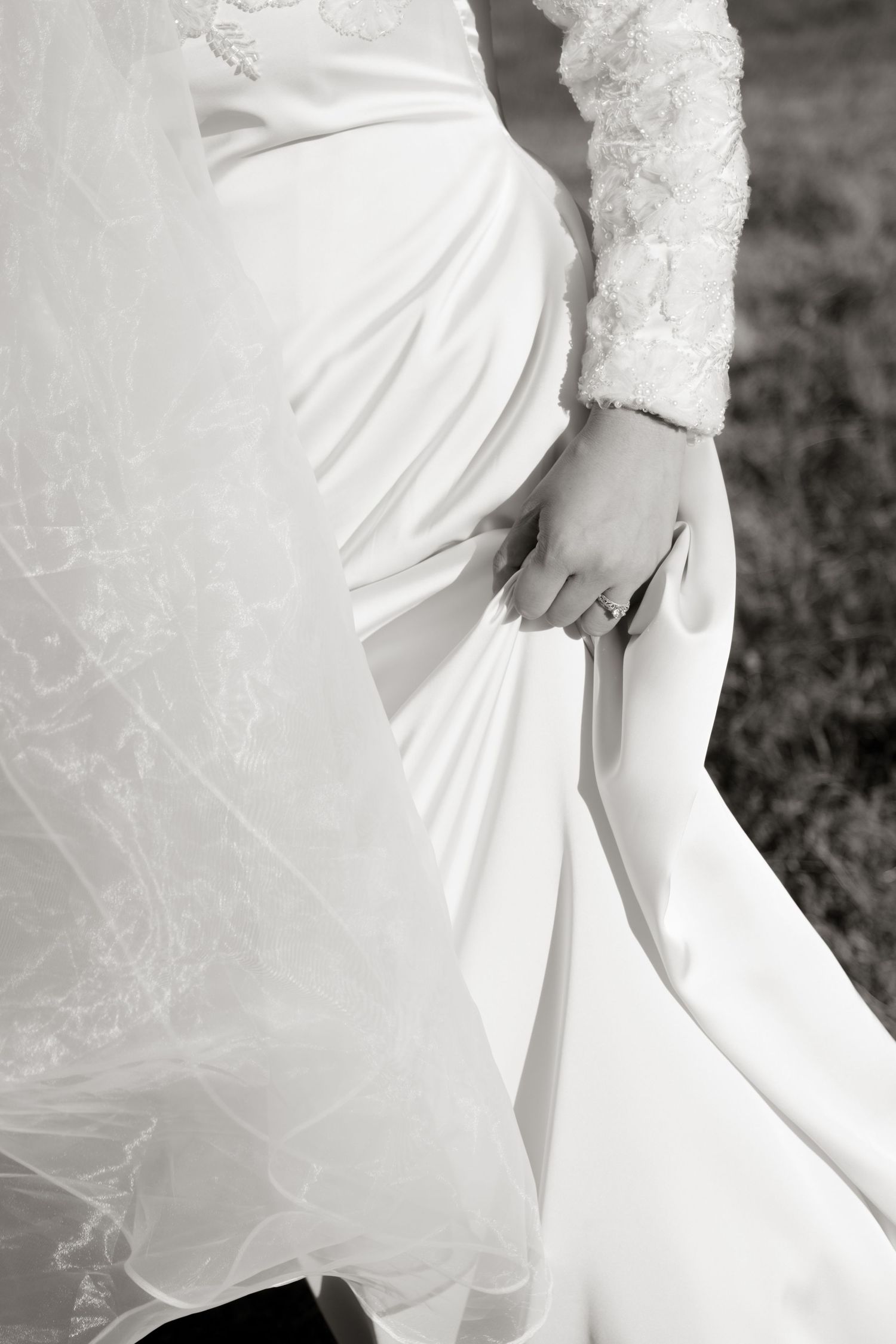 Close-up of a bride in a white lace wedding gown holding her dress, wearing a diamond ring.