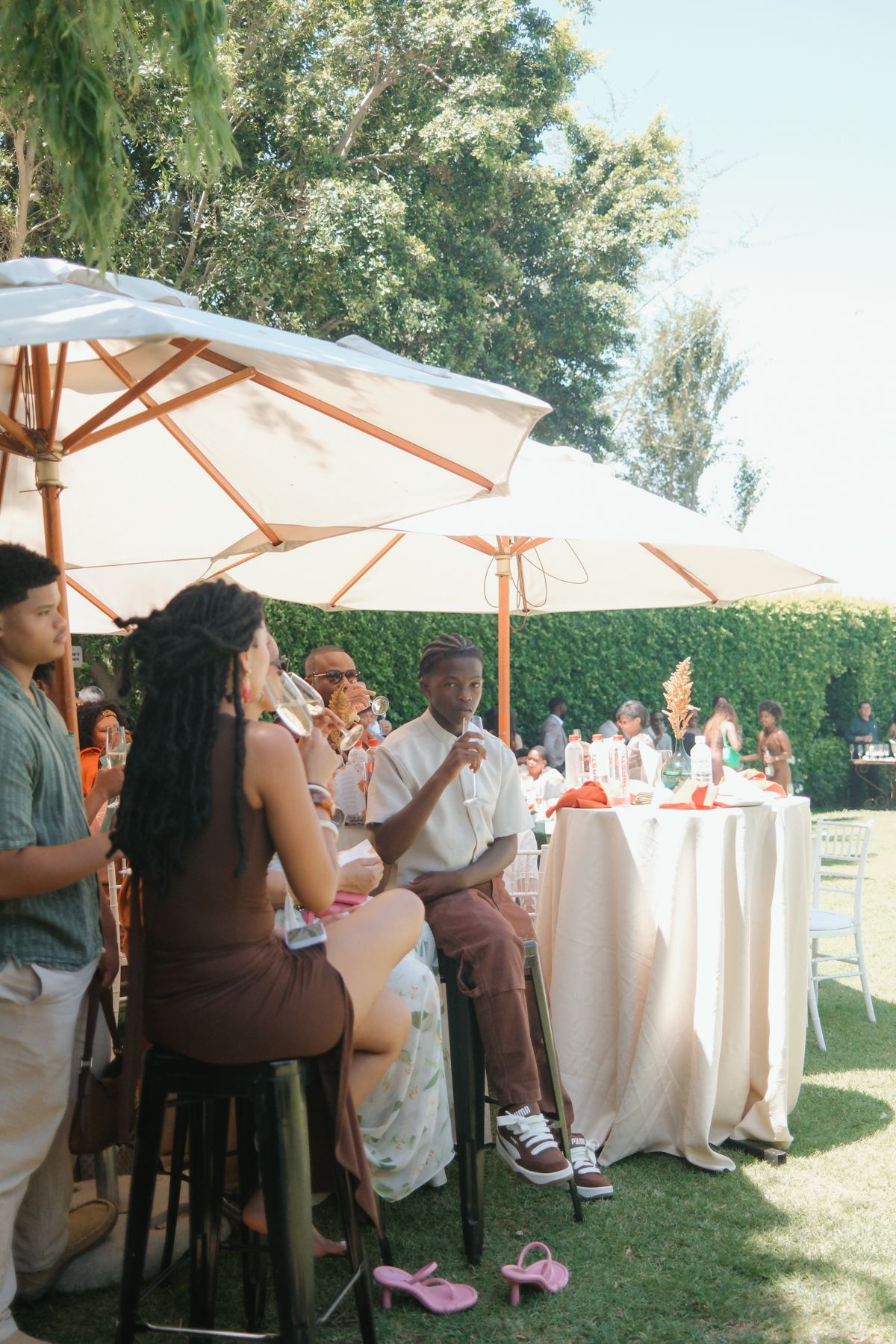 Guests socializing at an outdoor wedding reception under white patio umbrellas on a sunny day.