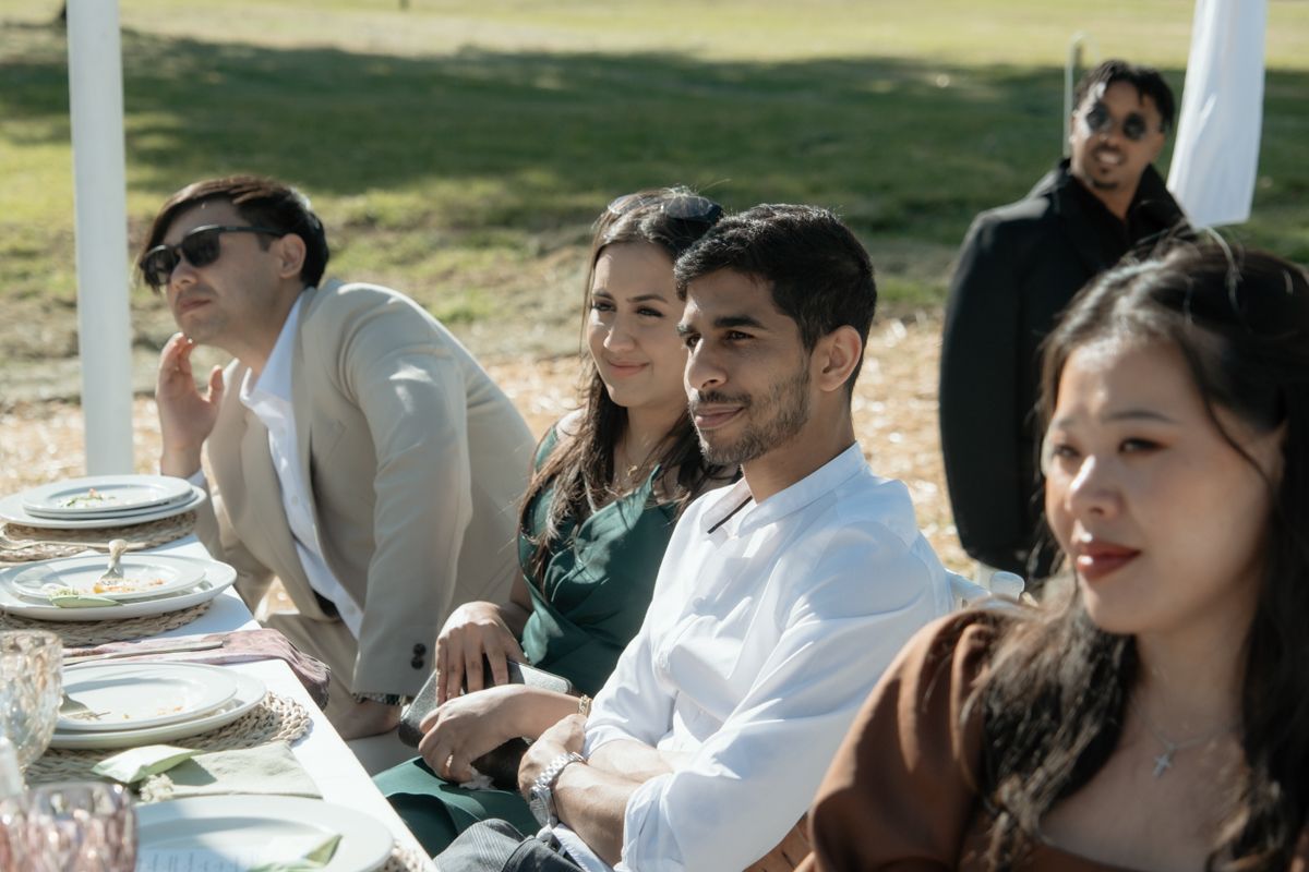 Guests seated outdoors at an elegant wedding reception table, smiling and enjoying the celebration.