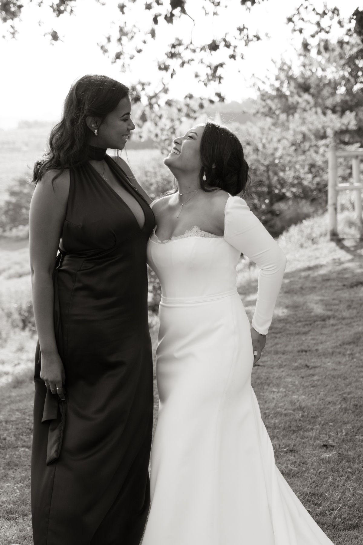 Black and white photo of a laughing bride in white gown sharing a joyful moment with her bridesmaid.