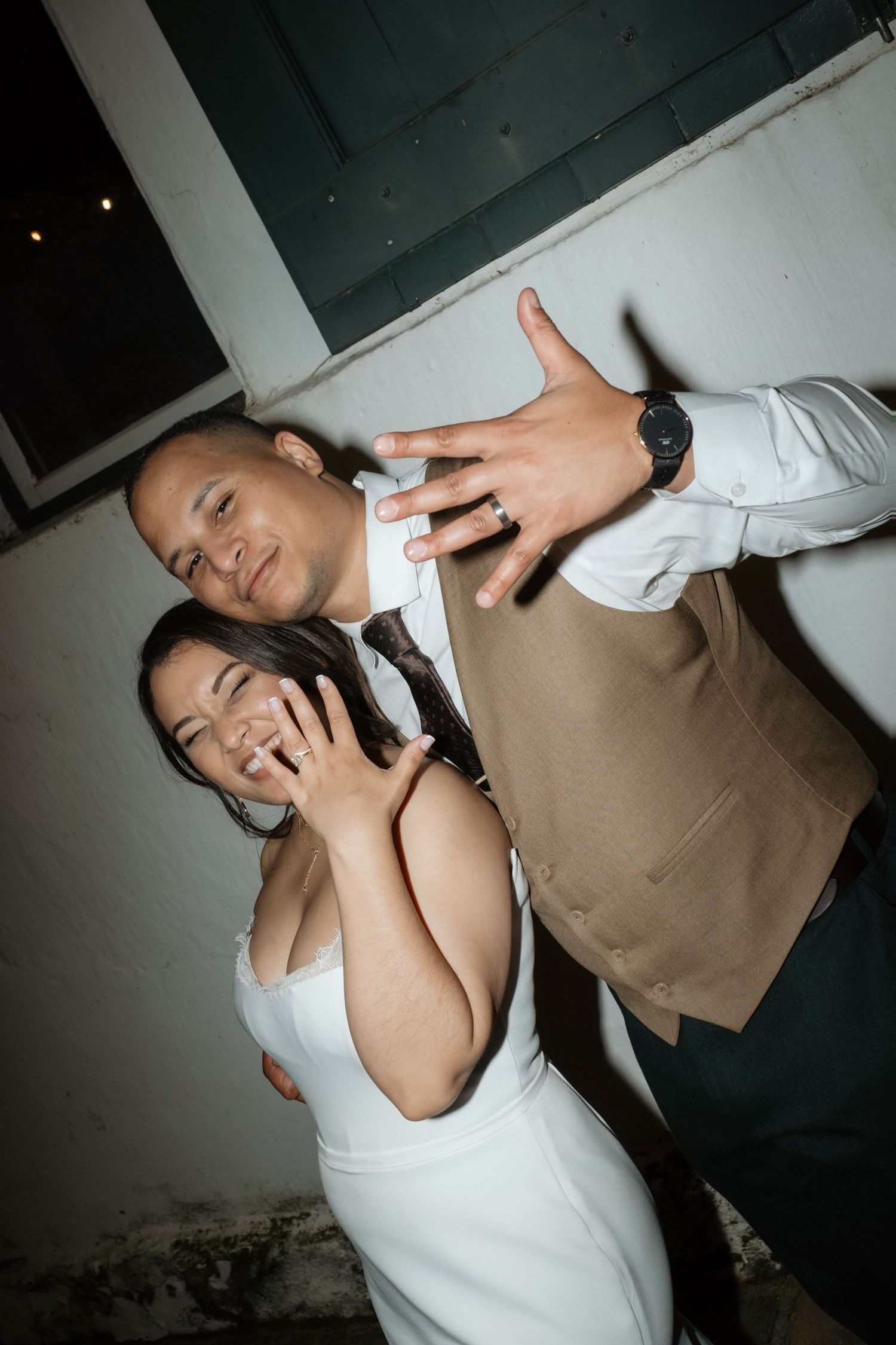 Joyful newlywed couple showing off wedding rings at outdoor reception celebration.