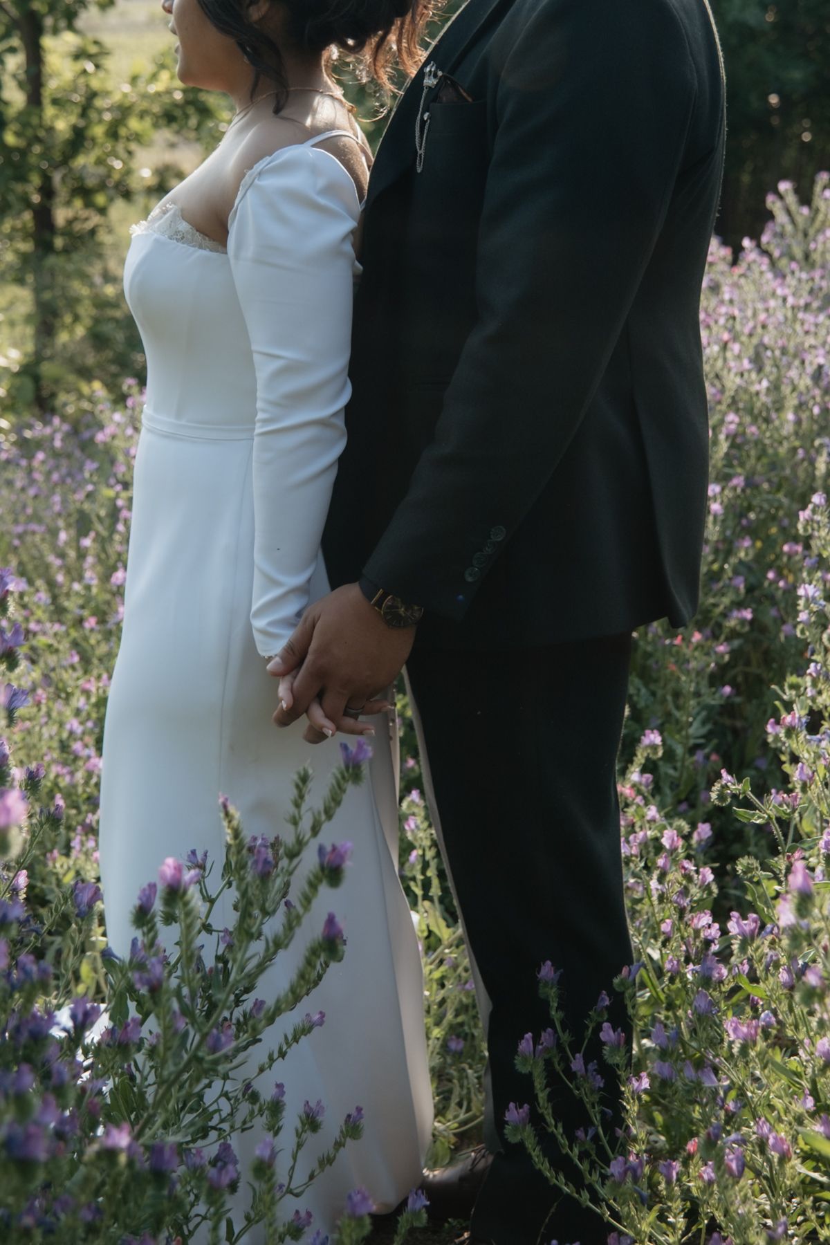 Bride and groom holding hands in purple wildflower field.