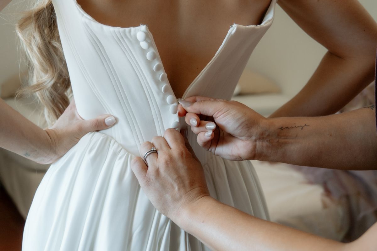 Bridesmaids helping button up the back of a white wedding dress before the ceremony.